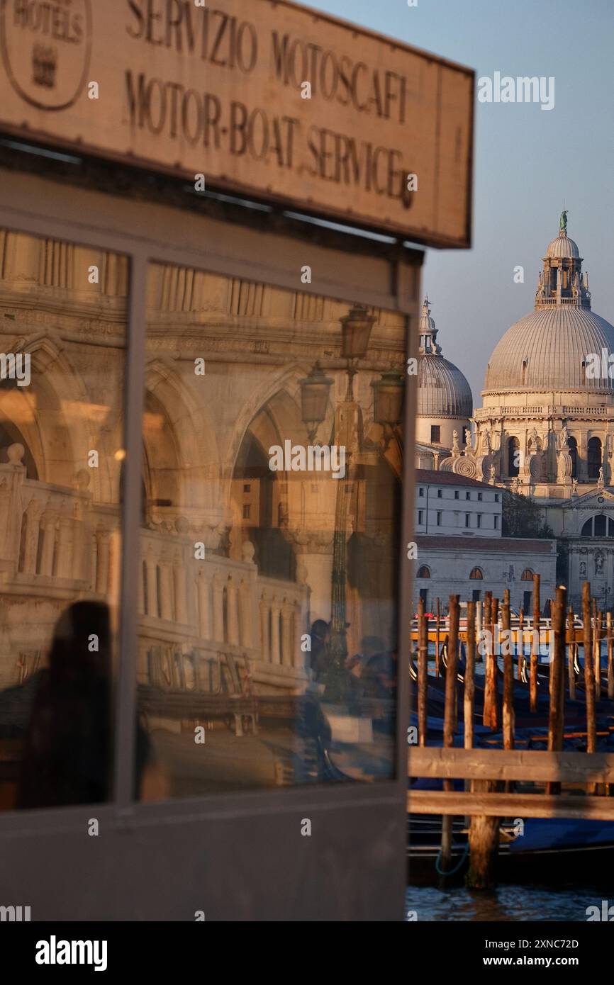 Venise, Italie, dômes de Santa Maria della Salute attrapant la lumière du soleil à l'aube et reflets du Palais des Doges dans le guichet du service de taxi à Molo Banque D'Images