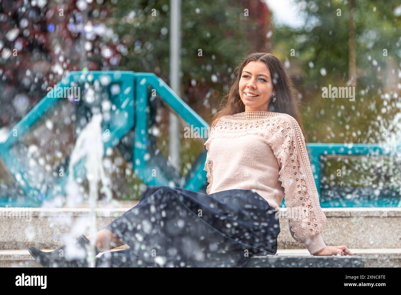 Une femme est assise près d'une fontaine étincelante, profitant de la lumière chaude du soleil. Banque D'Images