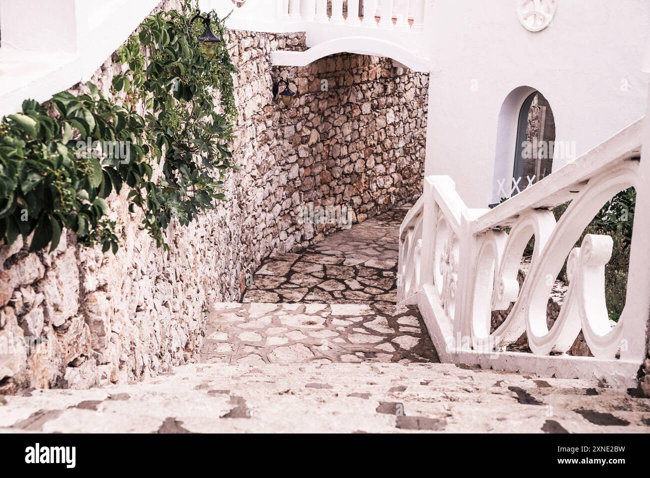 Un charmant sentier de pierre dans un hôtel italien, avec des murs rustiques, une végétation luxuriante et d'élégantes balustrades blanches. Banque D'Images
