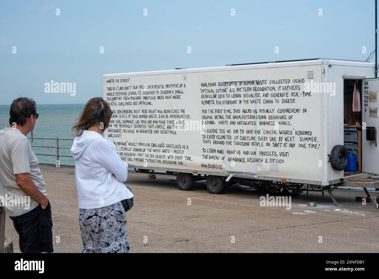 Margate, Royaume-Uni. 31 juillet 2024. Un couple a lu la description du projet sur le côté de la remorque au bord de la mer. Le Bureau of Abundance, Research & Design Ltd est une petite organisation environnementale basée au Royaume-Uni. Le Land Raft est leur premier prototype expérimental de studio de réponse mobile. Leur projet ambitieux est d’avoir 5 000 studios mobiles à partir de l’été prochain. (Photo de Krisztian Elek/SOPA images/SIPA USA) crédit : SIPA USA/Alamy Live News Banque D'Images