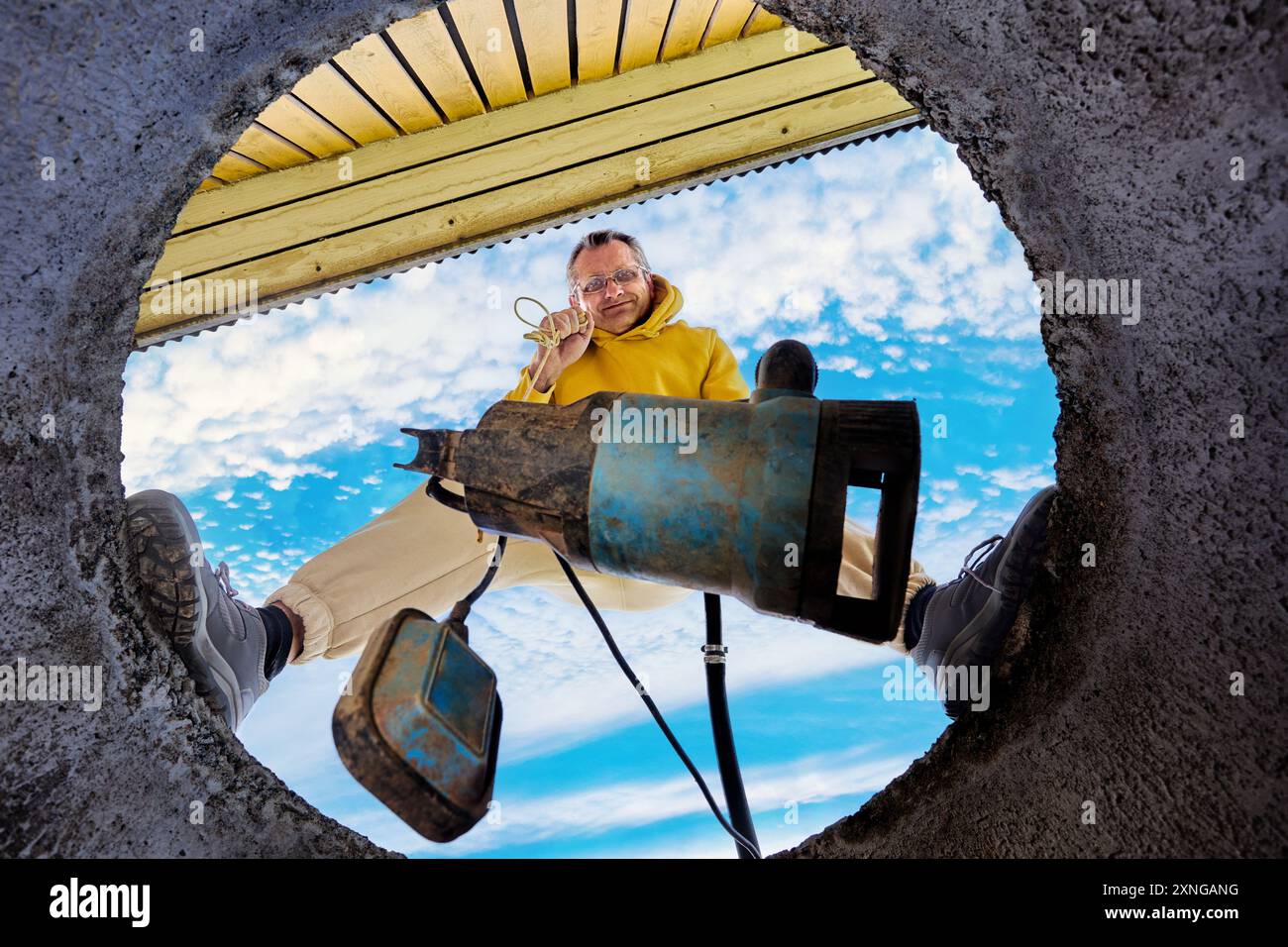 La pompe d'égout est immergée dans les eaux usées à travers l'anneau de béton du puits, vue de dessous de l'homme debout sur le bord de la fosse septique. Banque D'Images