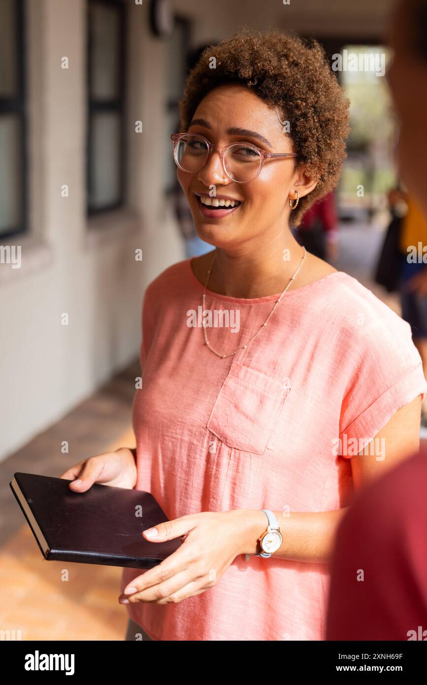 Adolescent souriant tenant un cahier, debout dans le couloir du lycée, portant des lunettes Banque D'Images