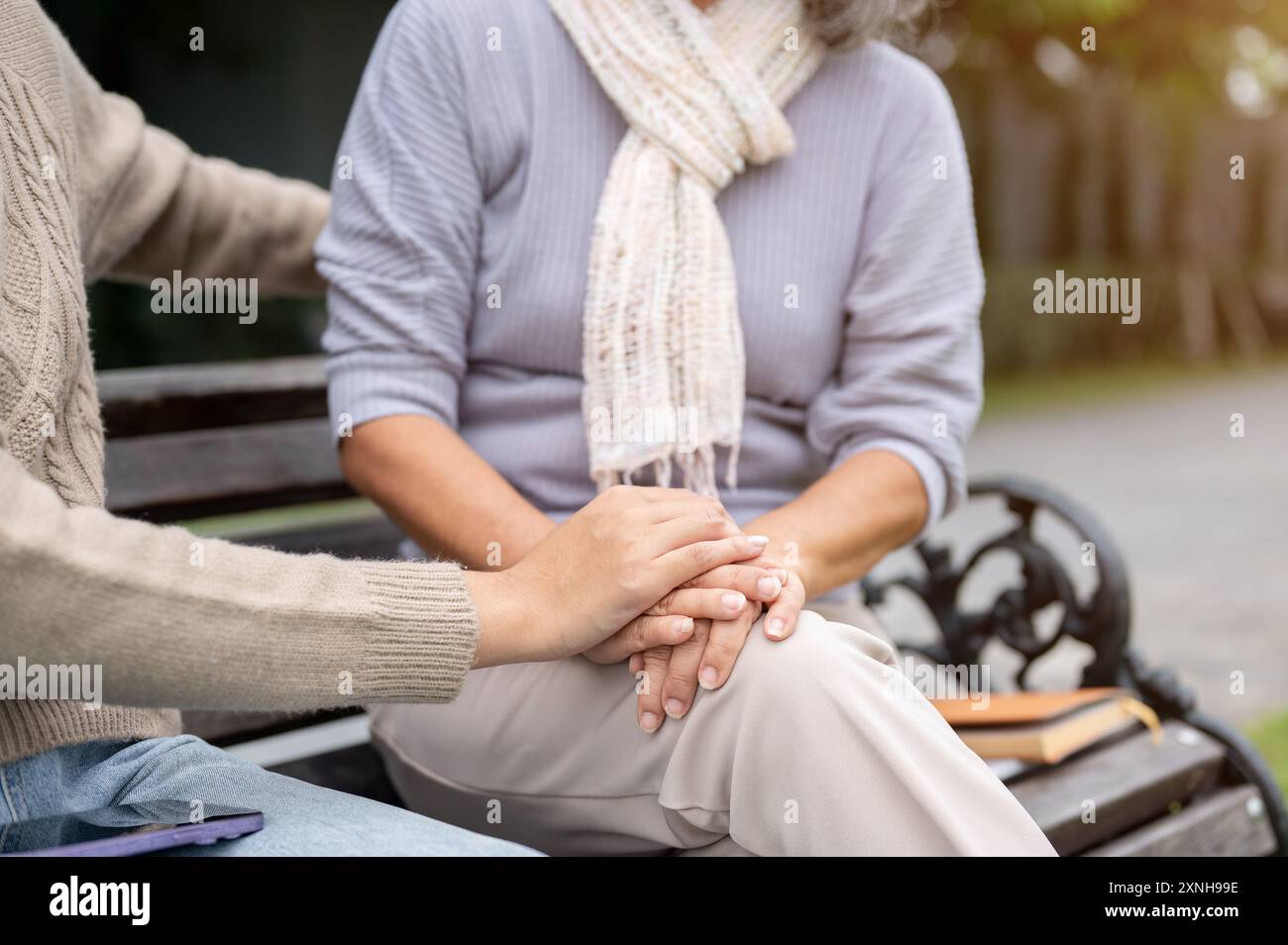 Une image en gros plan d'une fille attentionnée tenant la main de sa mère tout en parlant, à la fois assise sur un banc et passant du temps ensemble dans leur jardin. Banque D'Images