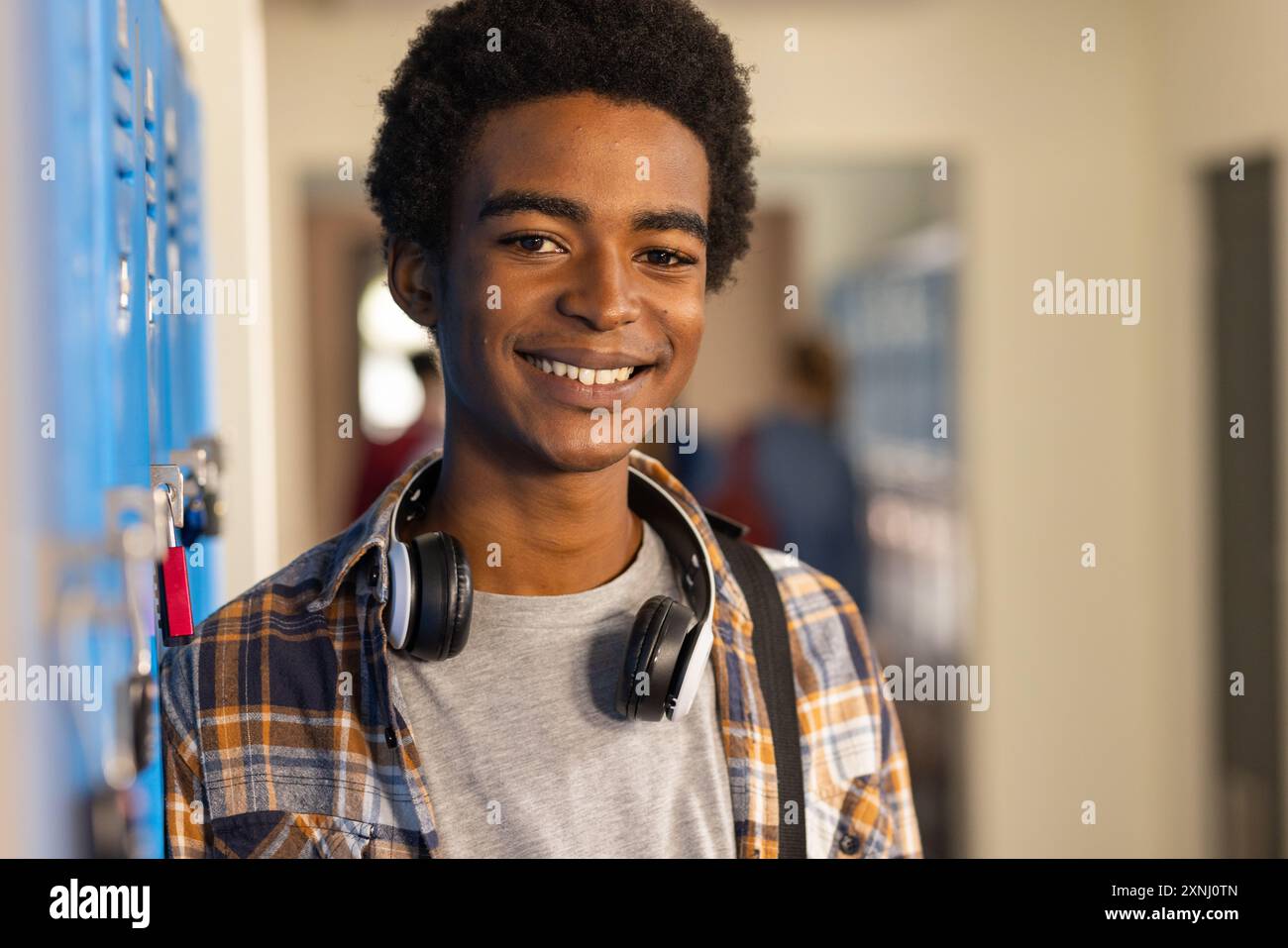 Adolescent souriant avec des écouteurs debout près de casiers dans le couloir du lycée Banque D'Images