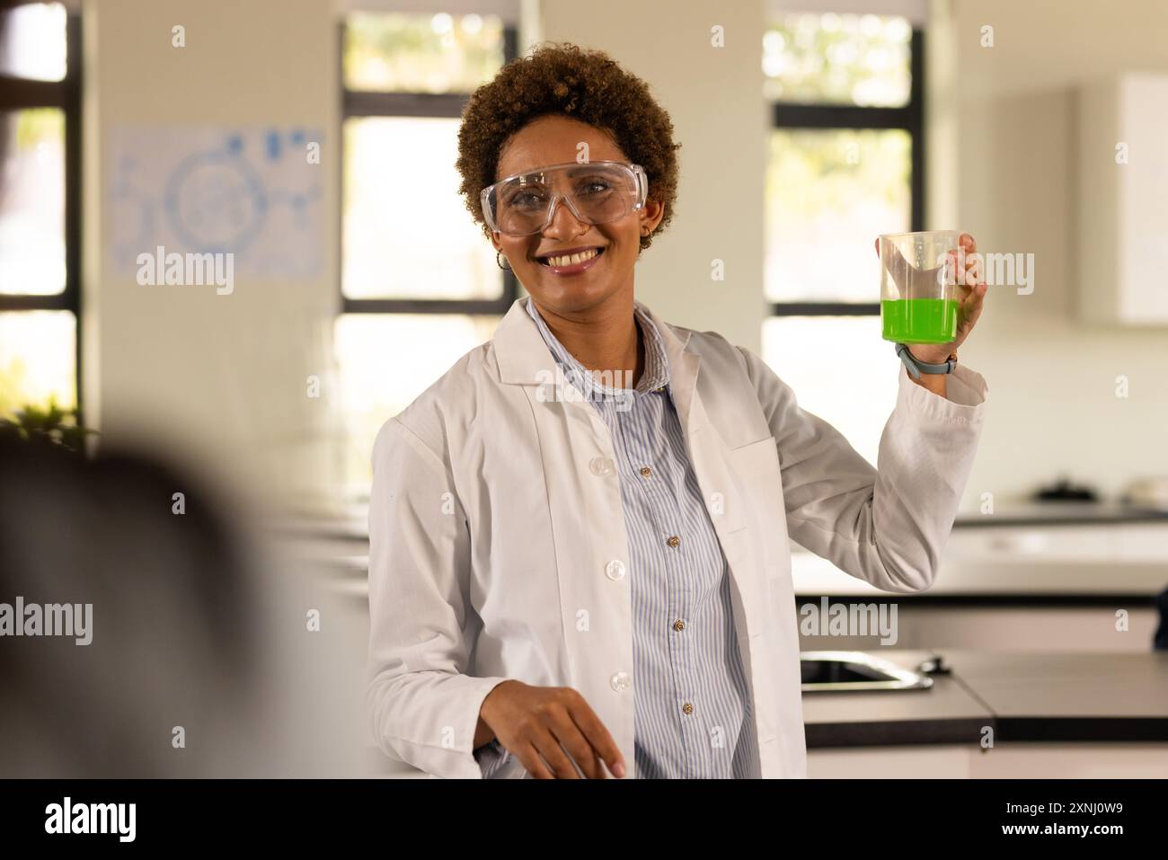 Au lycée, professeur tenant un bécher avec du liquide vert, souriant dans la classe de sciences Banque D'Images