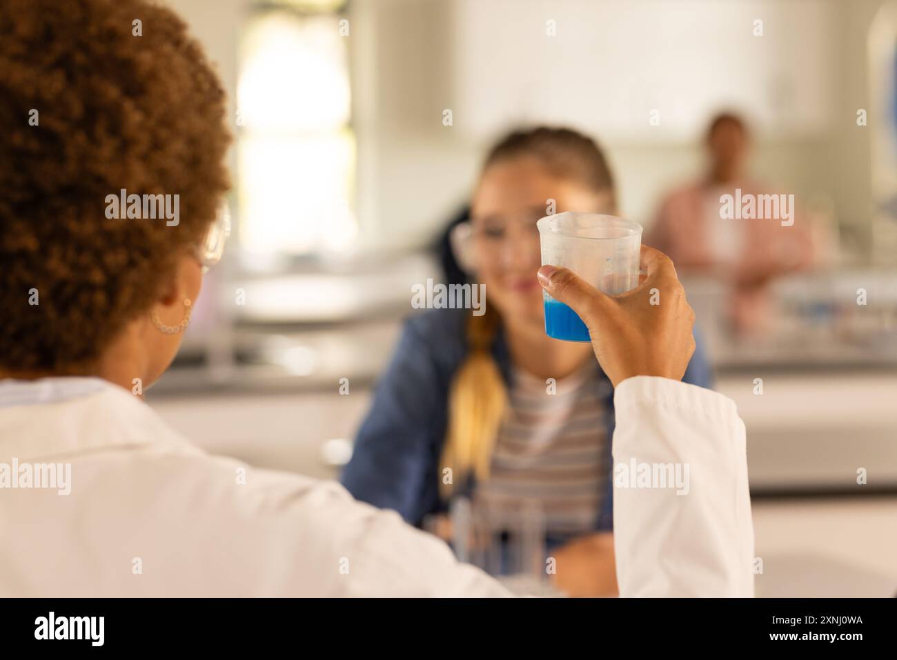 Au lycée, professeur tenant un bécher avec du liquide bleu, étudiant regardant attentivement Banque D'Images