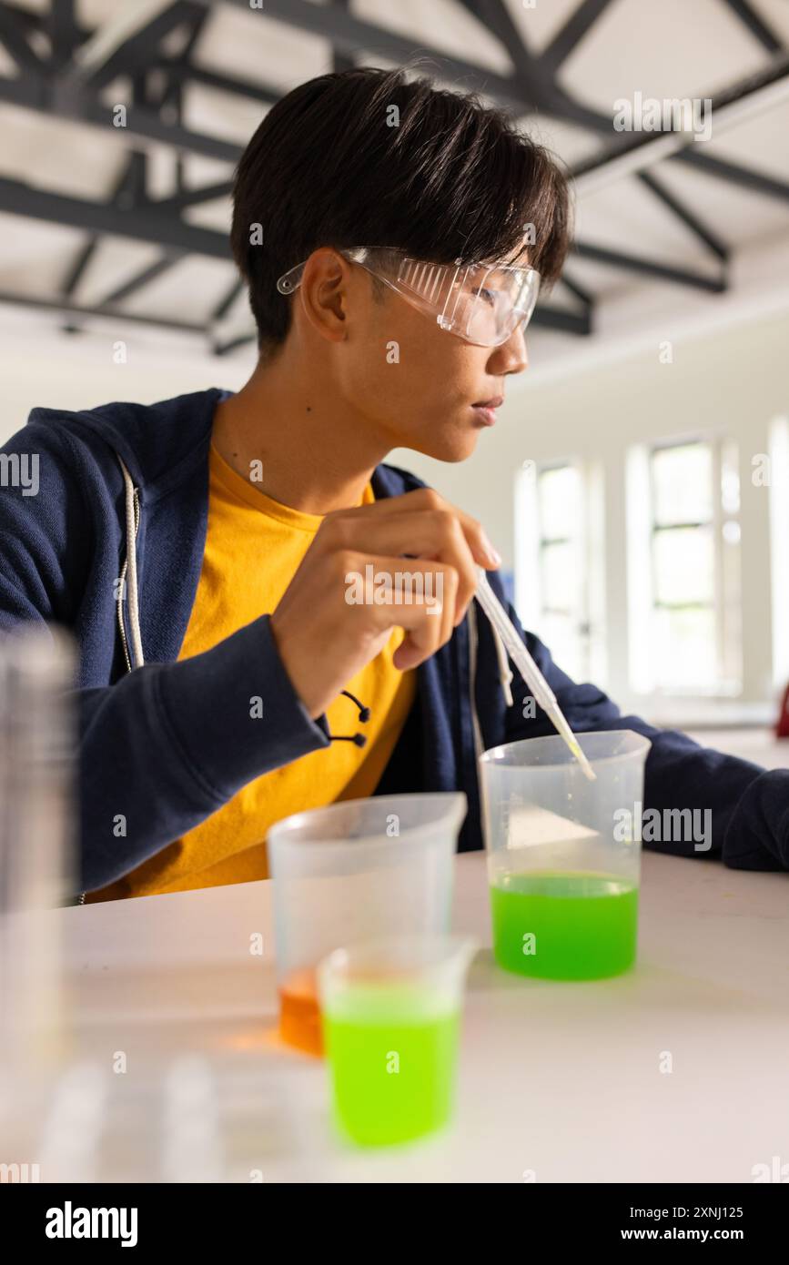 Mener une expérience scientifique avec des béchers et une pipette, adolescent en classe de lycée Banque D'Images