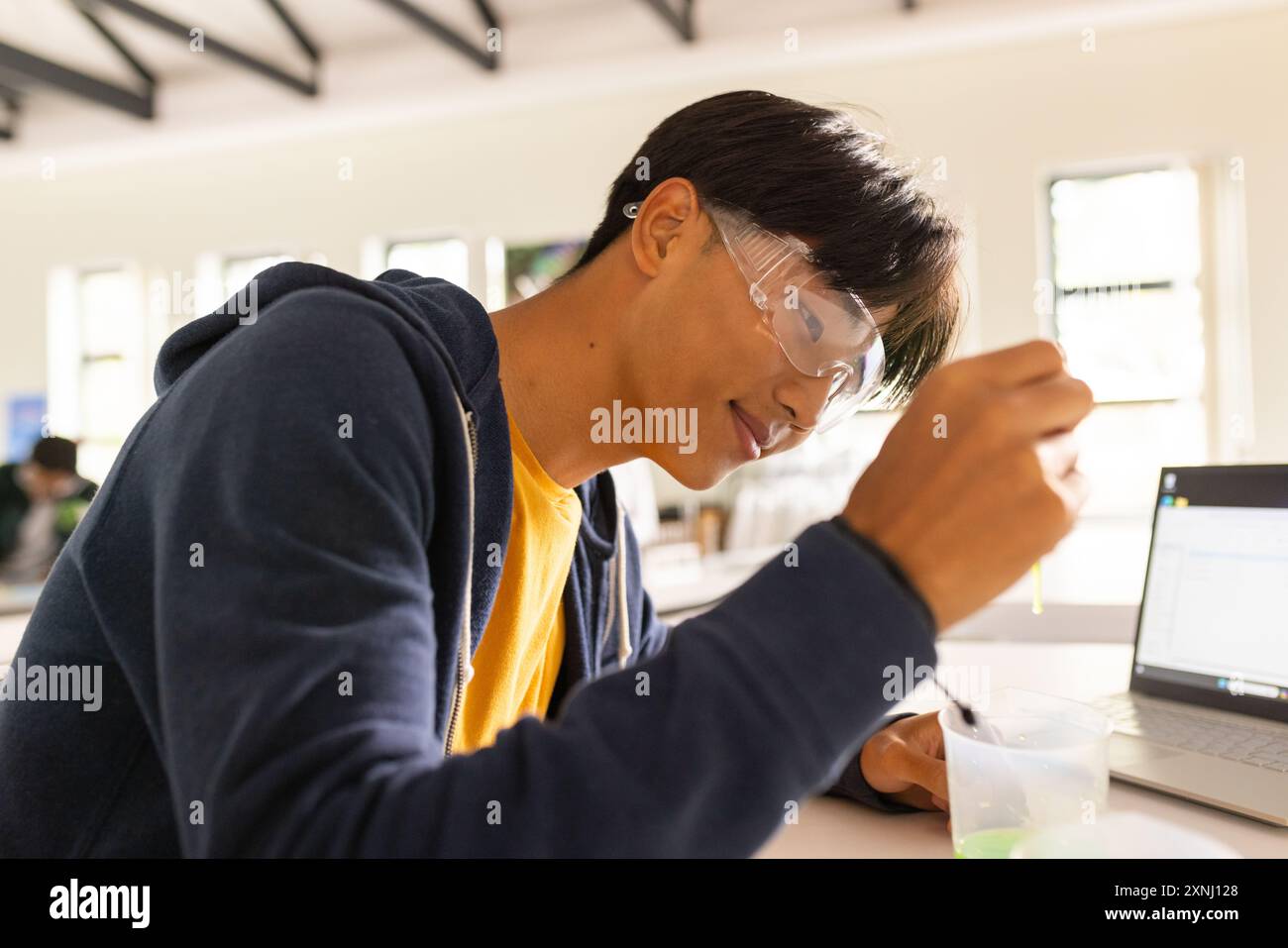 Au lycée, adolescent menant une expérience scientifique avec un ordinateur portable et des lunettes de sécurité Banque D'Images