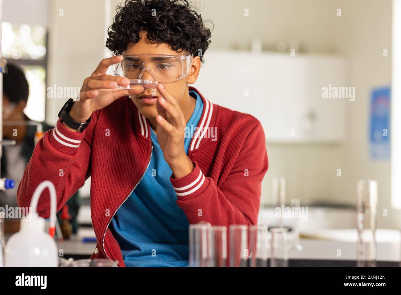 Au lycée, adolescent examinant un tube à essai dans une classe de sciences, portant des lunettes de sécurité Banque D'Images