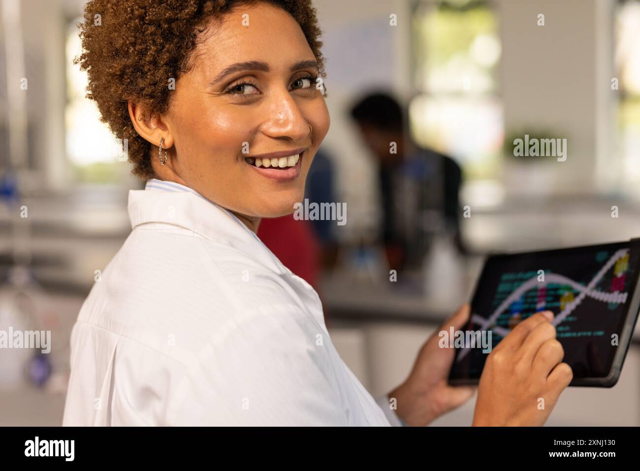 Au lycée, professeur souriant utilisant la tablette pour étudier la structure de l'ADN dans le laboratoire de science Banque D'Images