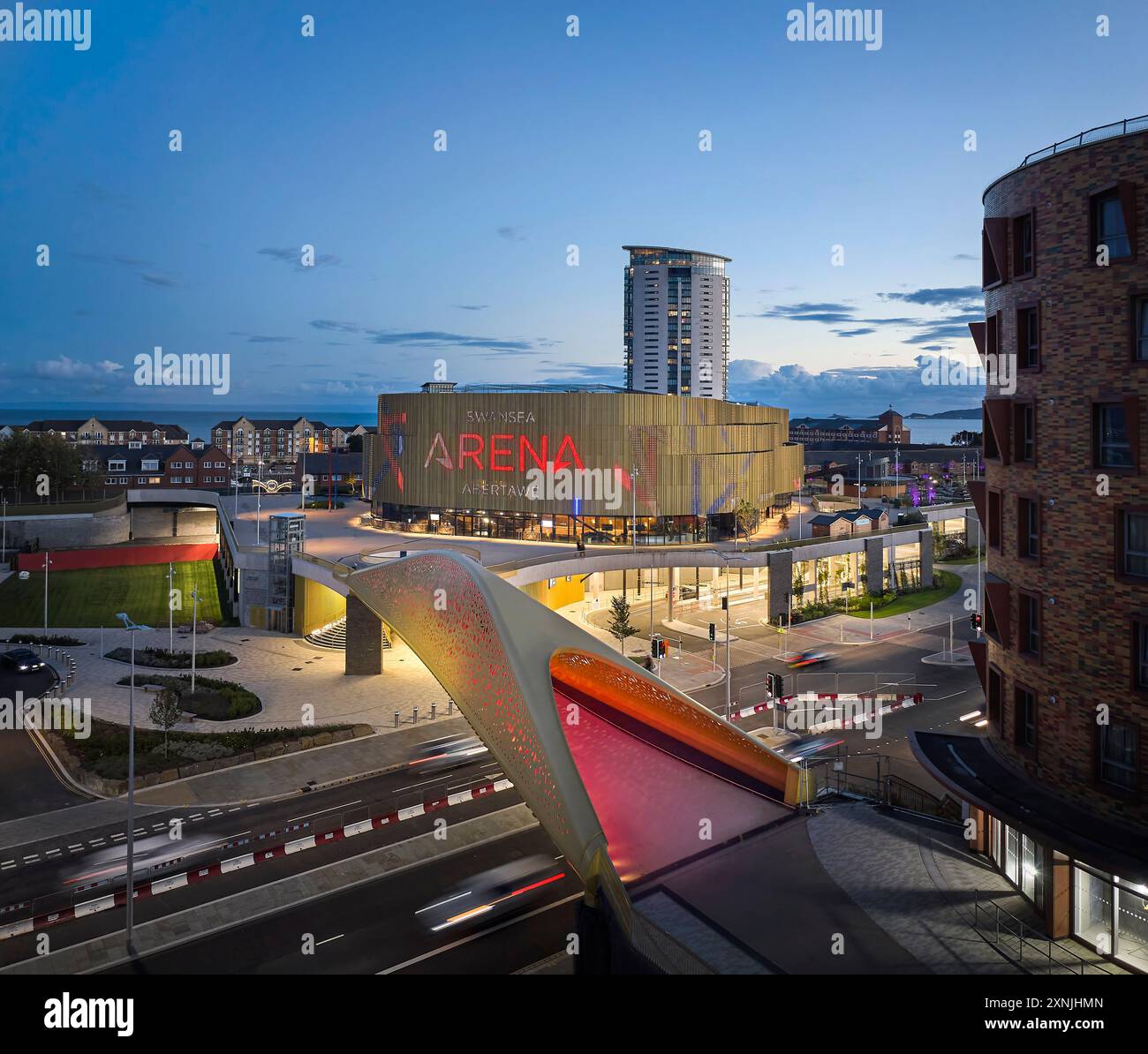 Pont et arène illuminés au crépuscule. Swansea Arena et Copr Bay Bridge, Swansea, Royaume-Uni. Architecte : acme, 2024. Banque D'Images