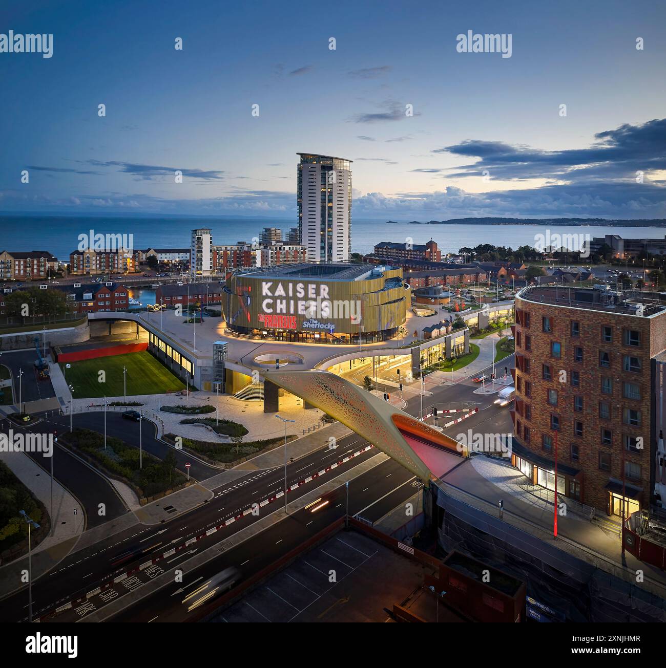 Pont et arène illuminés au crépuscule. Swansea Arena et Copr Bay Bridge, Swansea, Royaume-Uni. Architecte : acme, 2024. Banque D'Images