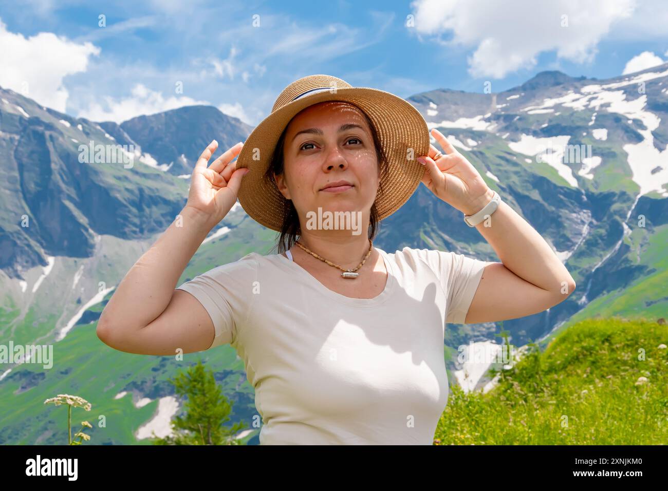 Une femme dans un chapeau de paille jouit d'une vue sur les montagnes alpines par une journée ensoleillée Banque D'Images