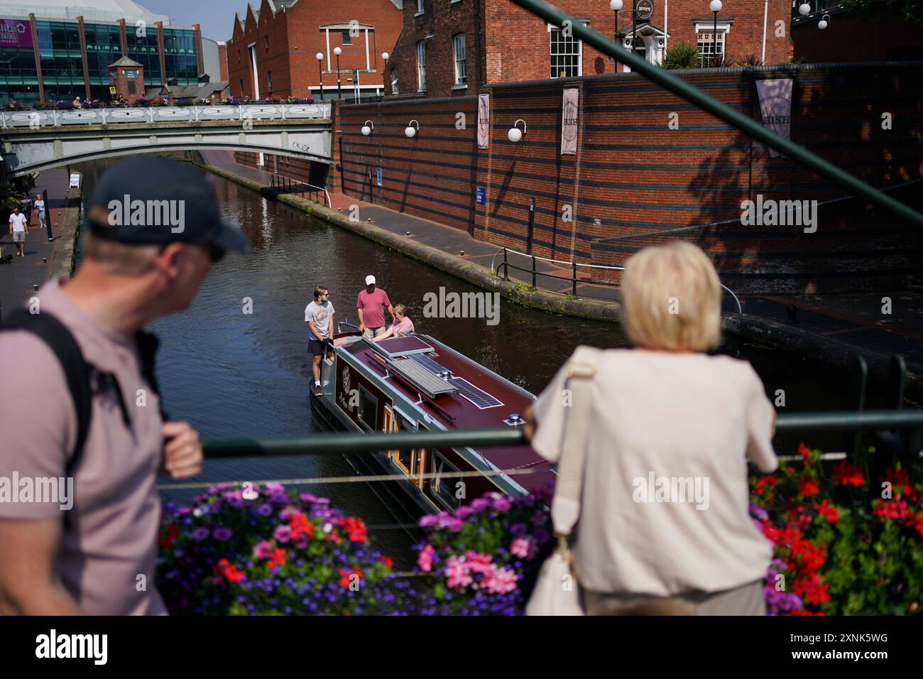 Les gens voyagent sur un canal en bateau étroit près de Brindleyplace à Birmingham. Les orages et les tempêtes de grêle devraient balayer certaines parties du Royaume-Uni jeudi alors que les températures atteignent 30 °C. Date de la photo : jeudi 1er août 2024. Banque D'Images