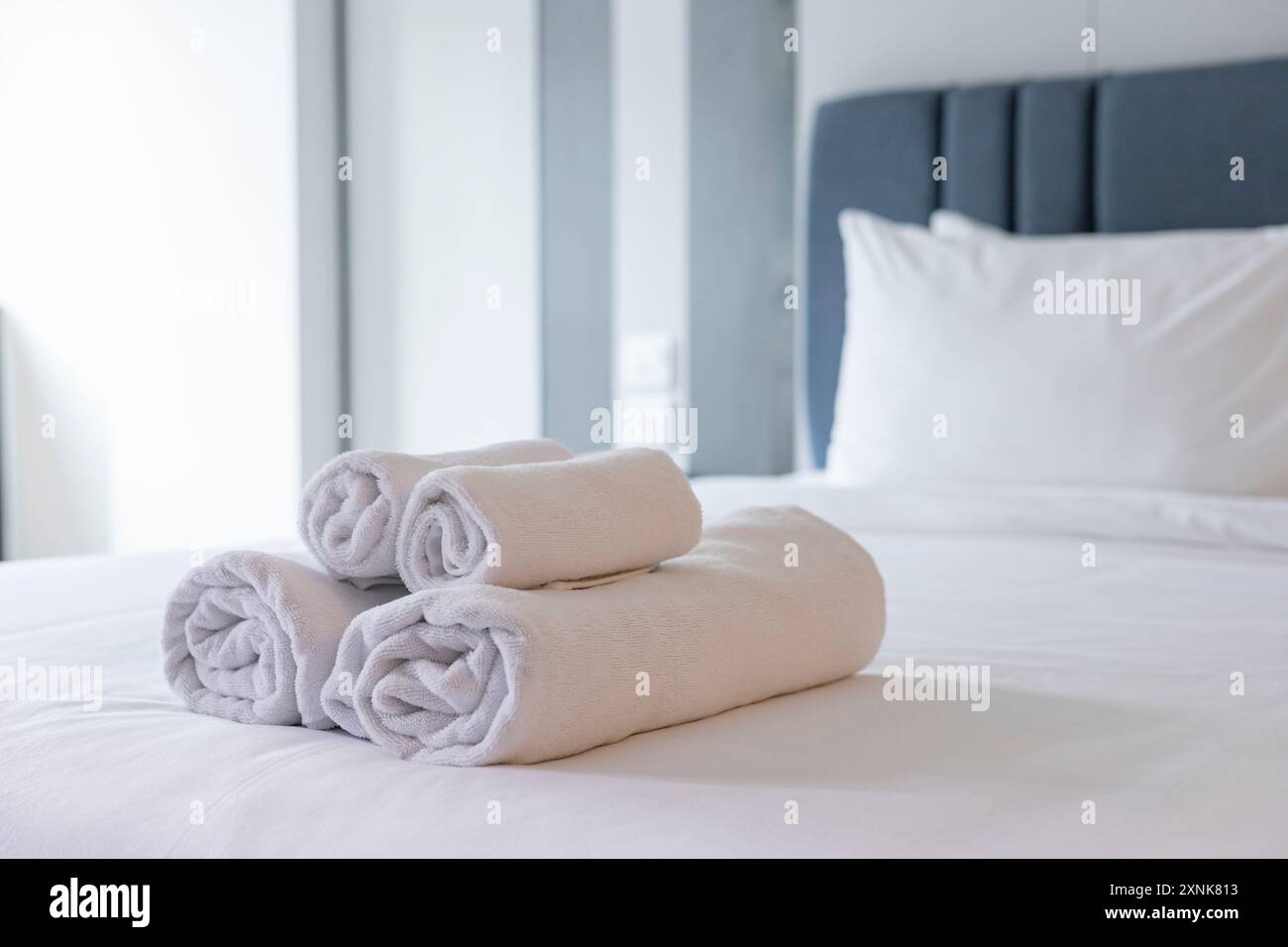 Serviettes blanches immaculées : soigneusement pliées et empilées sur un lit doux et propre dans une chambre d'hôtel confortable, mettant l'accent sur le luxe, le confort et l'hygiène Banque D'Images