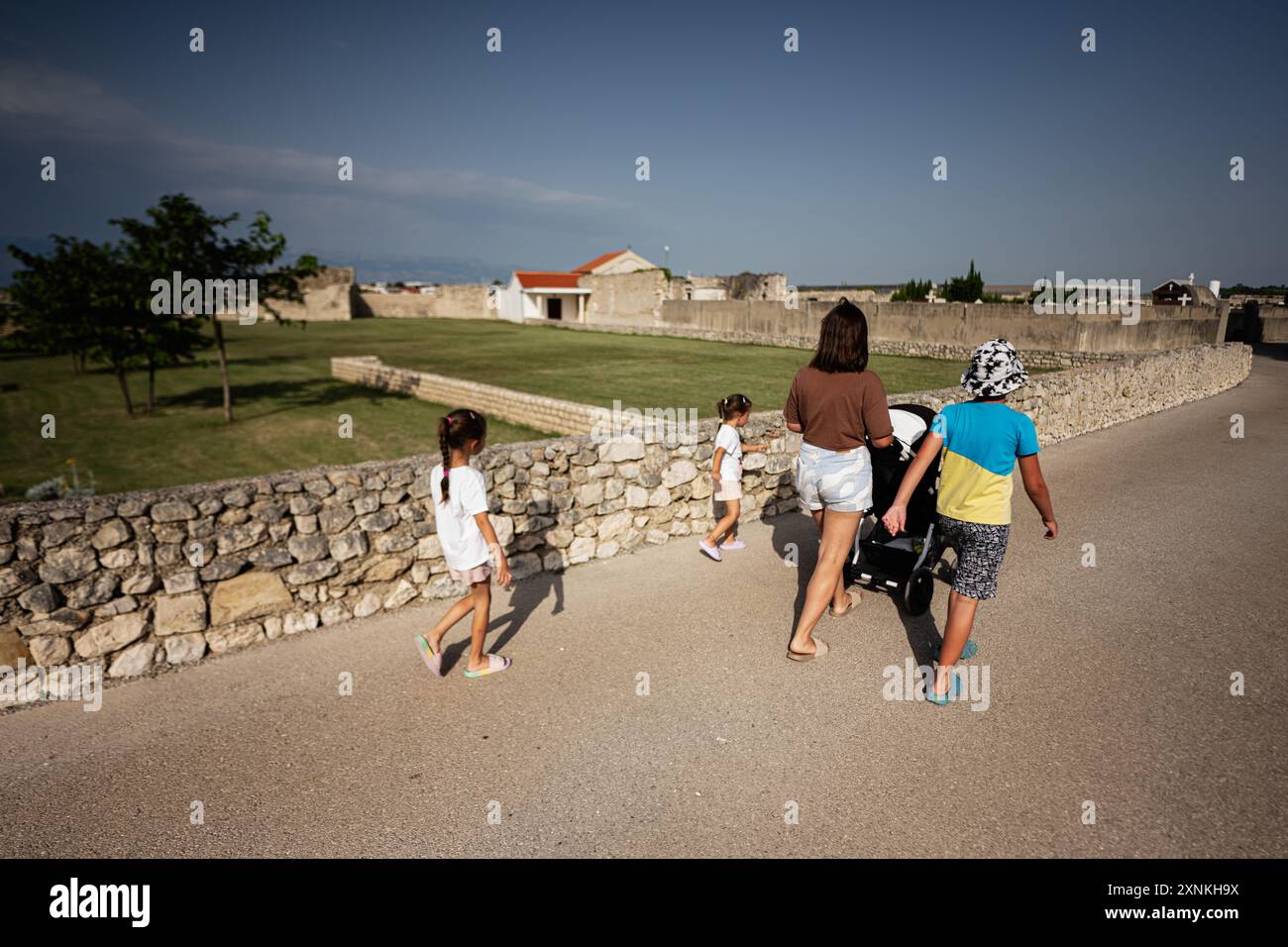 Une famille profite d'une journée ensoleillée de marche le long d'un mur de pierre sur un site historique. La mère pousse une poussette pendant que les enfants explorent les environs de Nin Banque D'Images