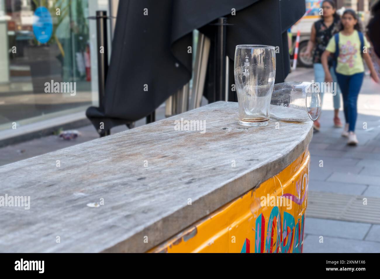 Verres vides laissés sur le comptoir du bar extérieur dans la rue de la ville avec les piétons qui passent devant. Banque D'Images