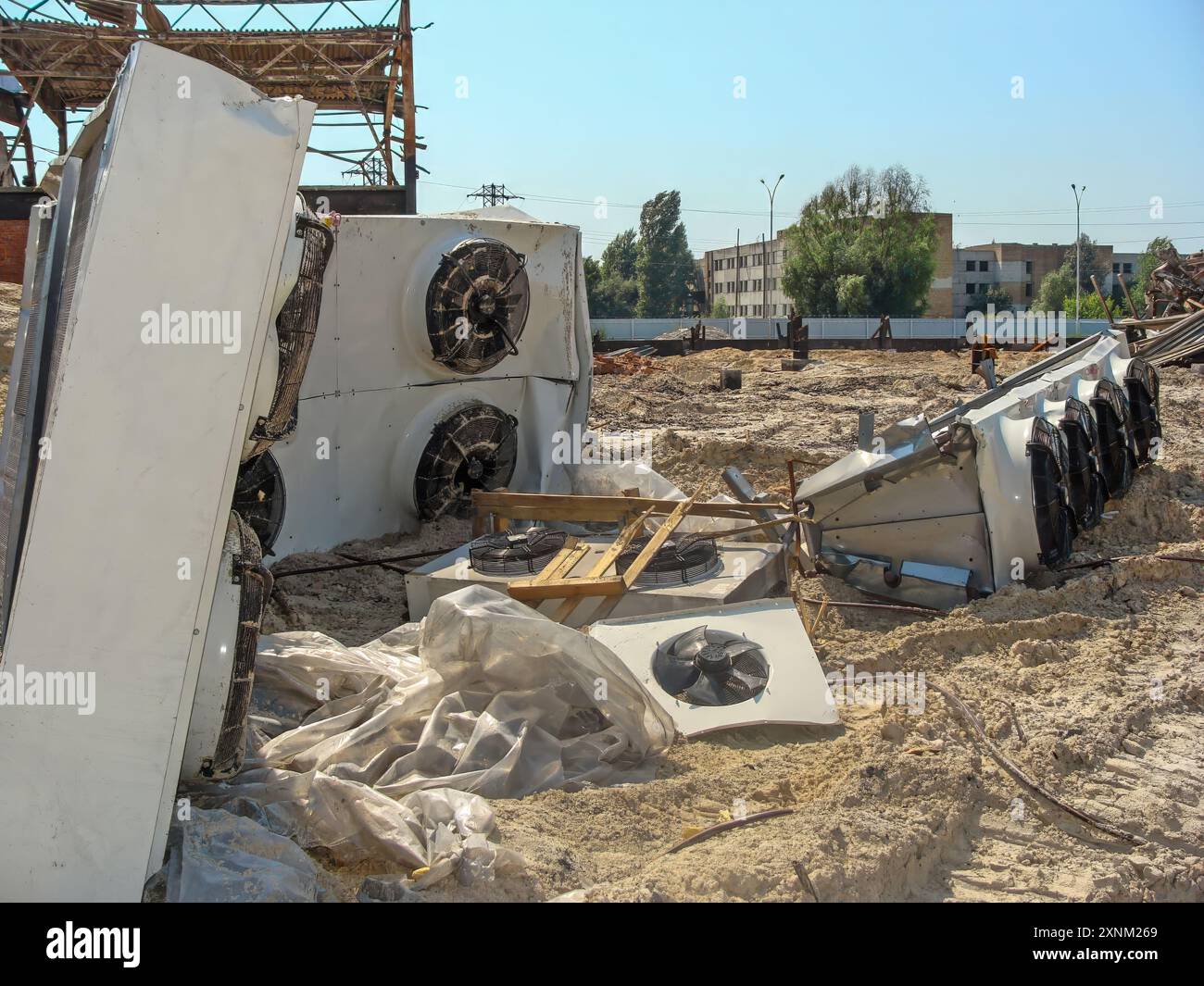 Ventilateurs industriels endommagés et débris sur un chantier de construction, avec une structure partiellement détruite en arrière-plan. Banque D'Images