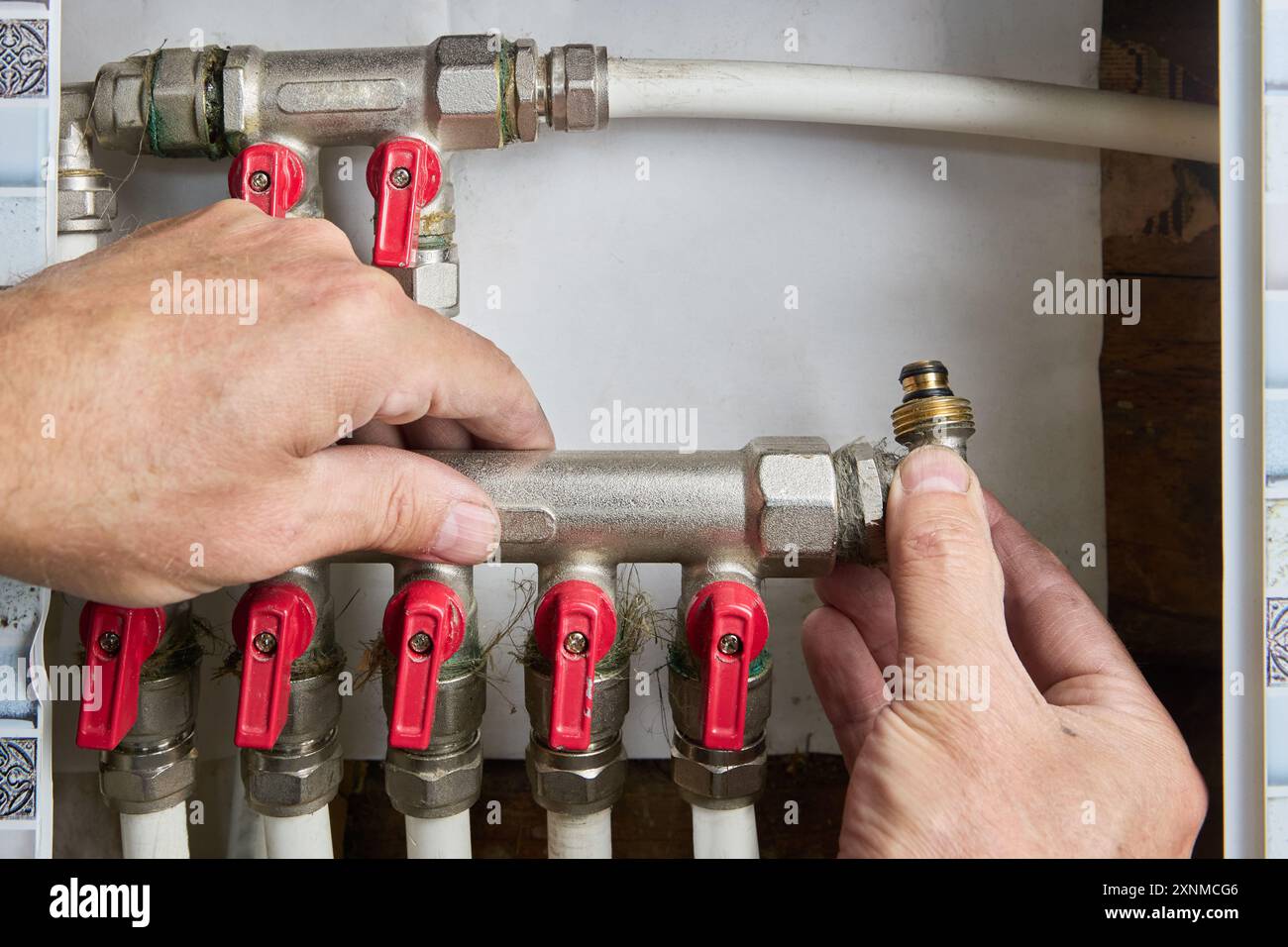 Plombier réparant collecteur de distribution d'eau, collecteur de tuyau avec vanne de commande manuelle dans le système domestique d'approvisionnement en eau. Banque D'Images