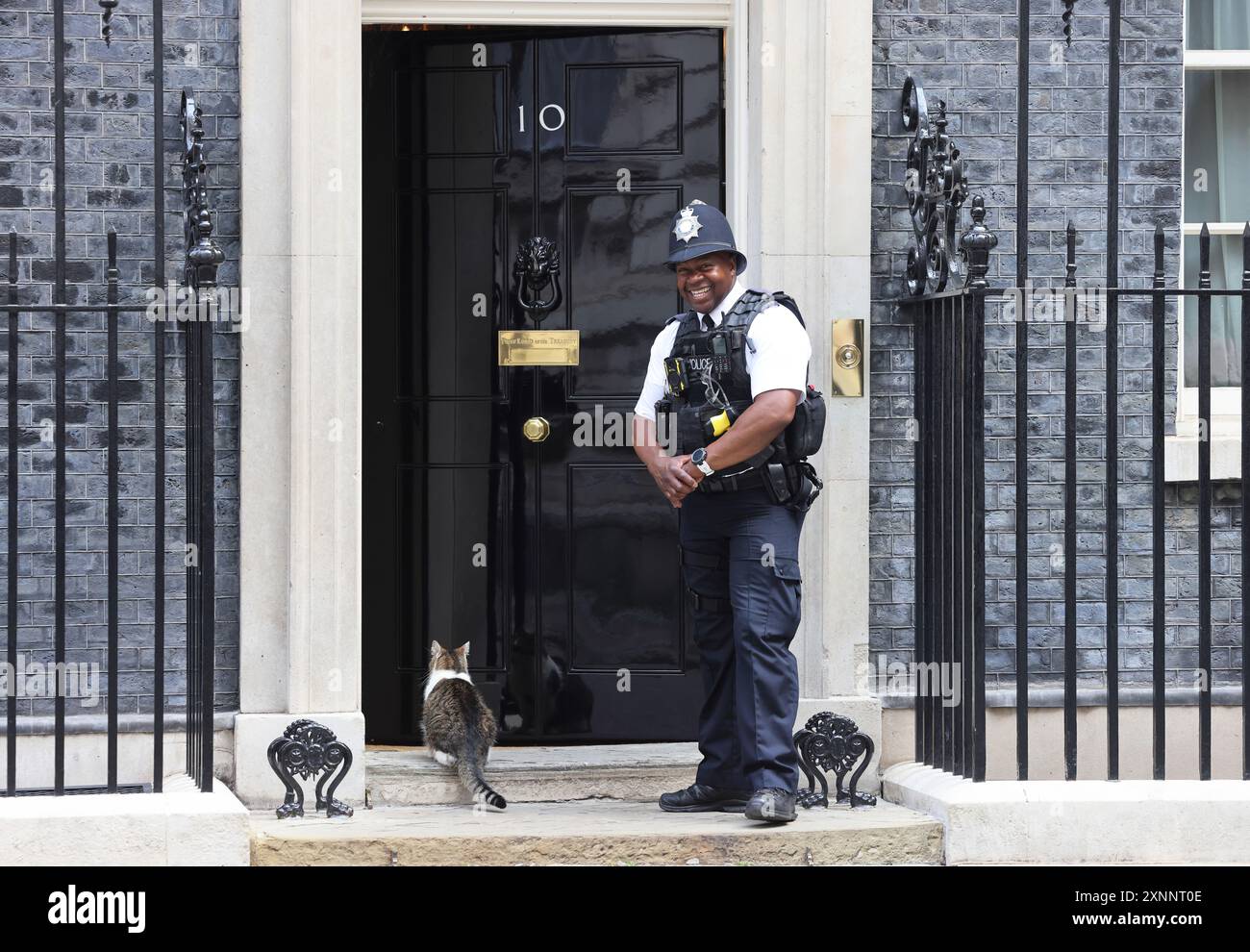 Larry le receveur de souris résident No.10 attendant d'être laissé entrer par British bobby sur Downing Street, Westminster, Londres, Royaume-Uni Banque D'Images