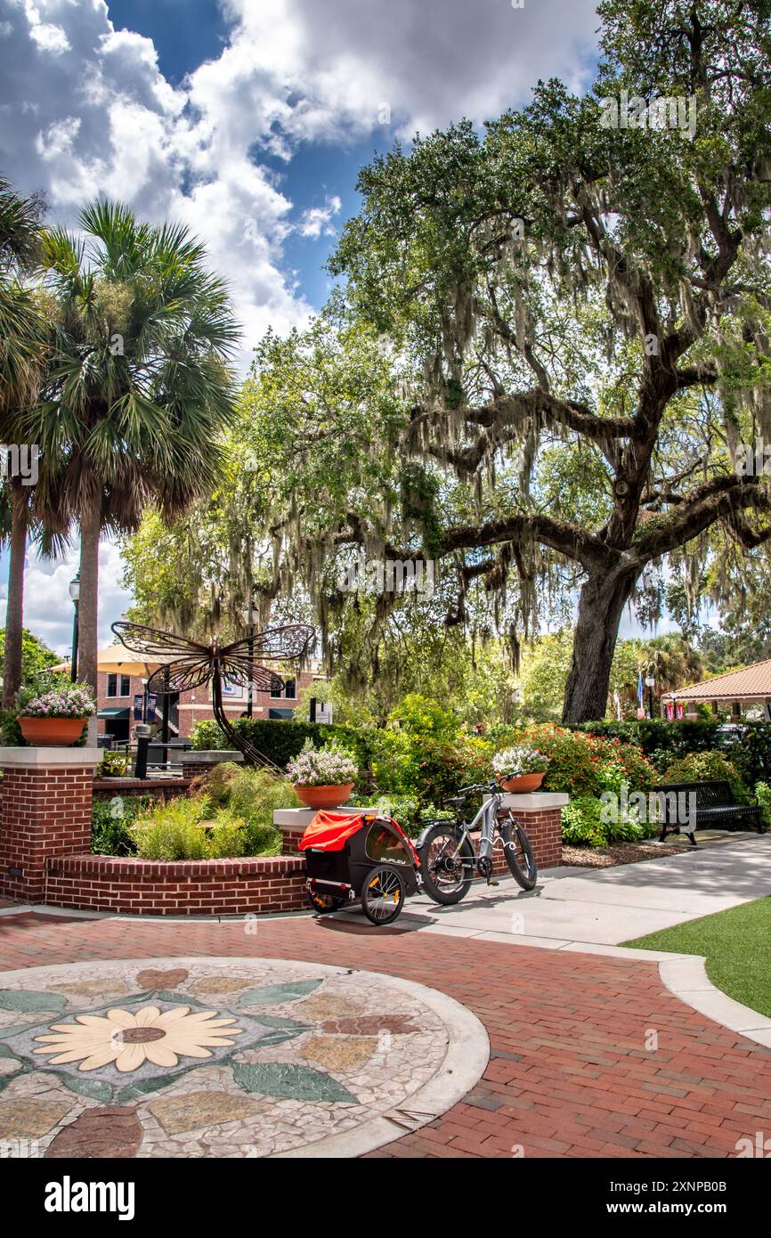 Vélo électrique à pneus gras avec remorque de vélo pour enfant garée par une sculpture de libellule dans le centre-ville Winter Garden, en Floride Banque D'Images