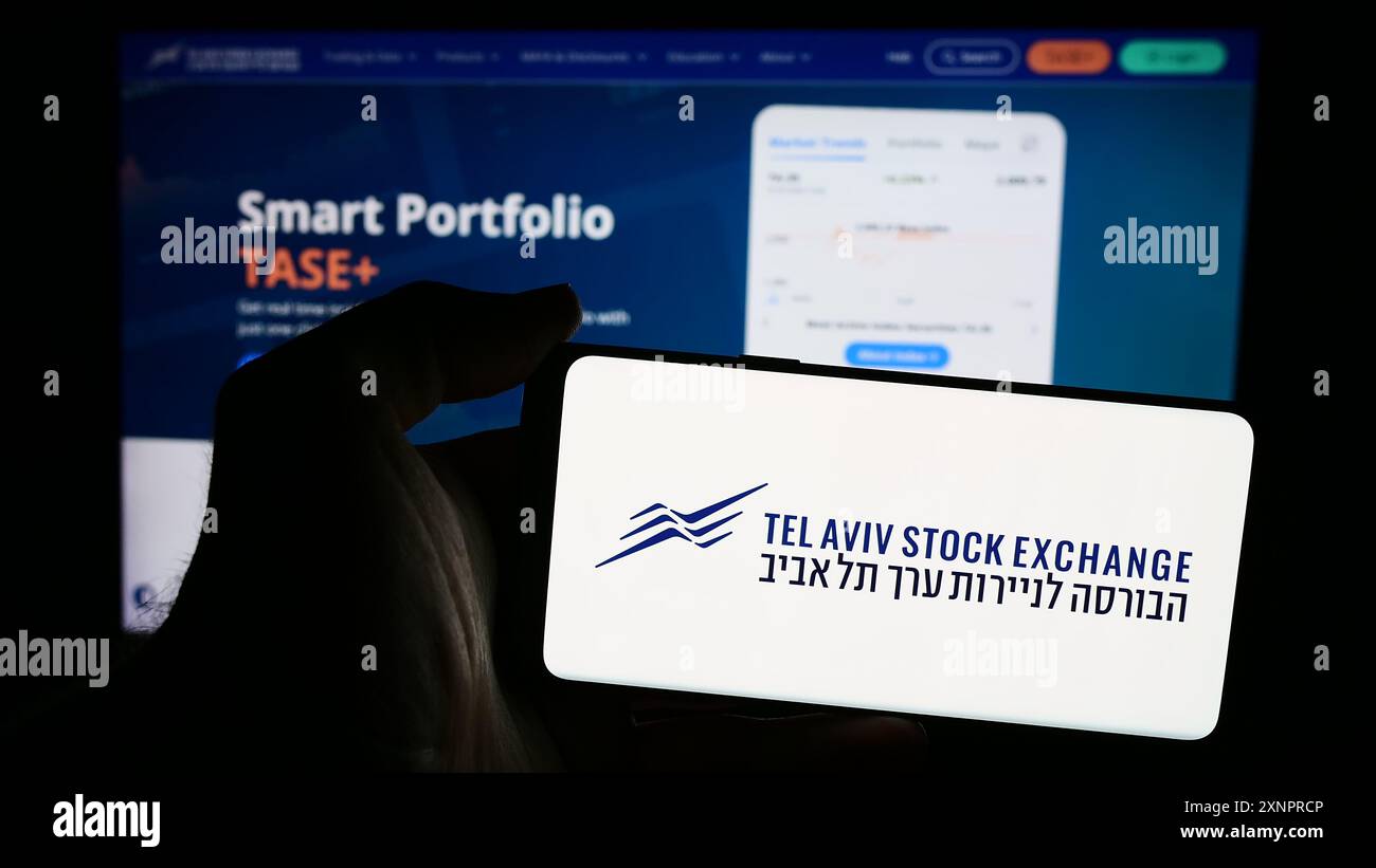 Personne tenant un smartphone avec le logo de la société israélienne tel Aviv Stock Exchange (TASE) en face du site. Concentrez-vous sur l'affichage du téléphone. Banque D'Images