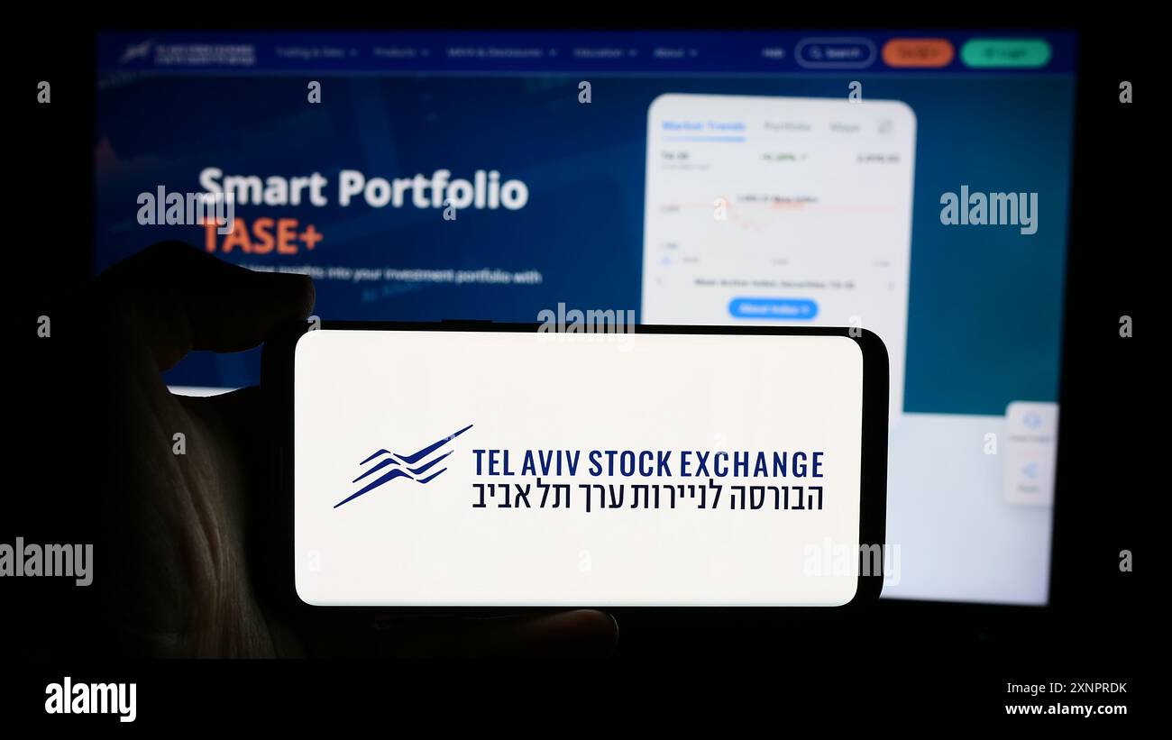 Personne tenant le téléphone portable avec le logo de la société israélienne tel Aviv Stock Exchange (TASE) en face de la page Web de l'entreprise. Concentrez-vous sur l'affichage du téléphone. Banque D'Images