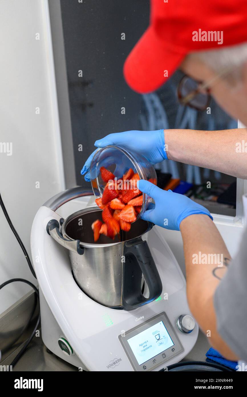 Une personne portant des gants bleus verse des fraises fraîches dans un appareil de cuisine moderne. L'appareil est un appareil de cuisson multifonction, avec Banque D'Images