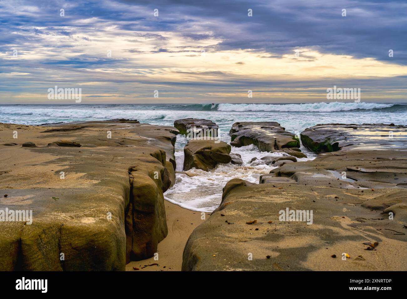 RIVAGE ROCHEUX AVEC UNE VAGUE TISSANT À TRAVERS LES OUVERTURES AVEC DES VAGUES EN ARRIÈRE-PLAN AVEC UN BEAU CIEL À LA JOLLA CALIFORNIE PRÈS DE SAN DIEGO Banque D'Images