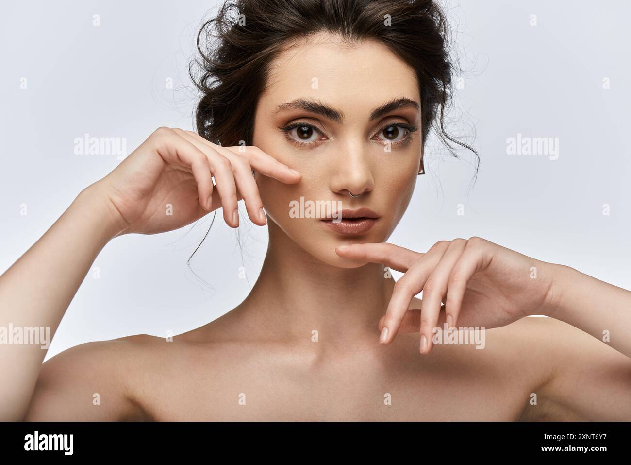 Gros plan de la jeune femme avec les cheveux foncés et la tenue élégante, mains encadrant le visage. Banque D'Images