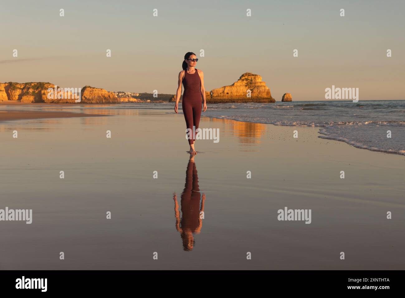 Femme sportive marchant le long d'une plage vide à marée basse. Banque D'Images