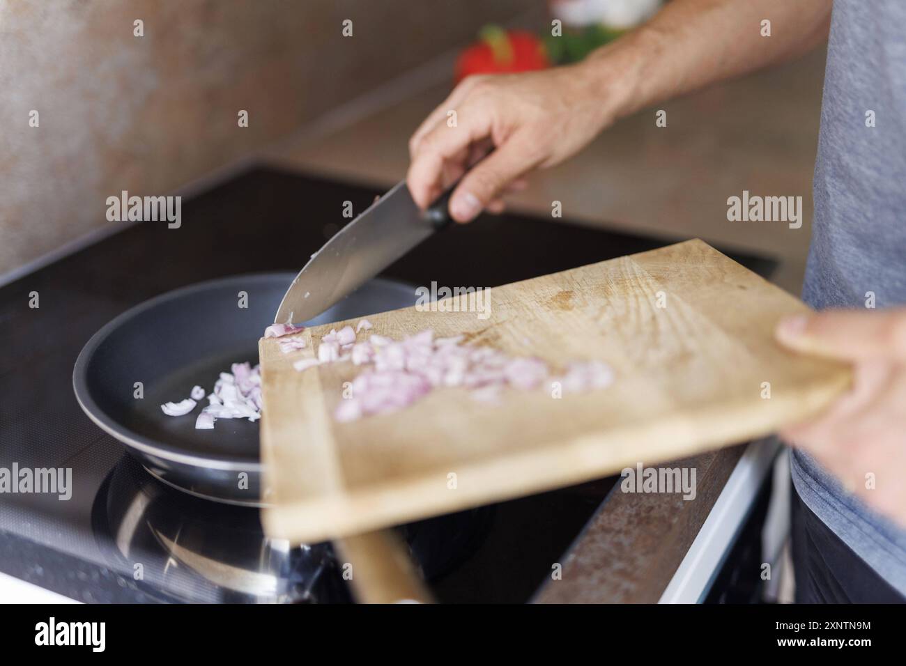 Thema kochen. Ein Mann schiebt Zwiebeln in eine Pfanne, um sie anzubraten. Berlin, 01.08.2024. Berlin Deutschland *** thème de cuisine Un homme pousse l'oignon Banque D'Images