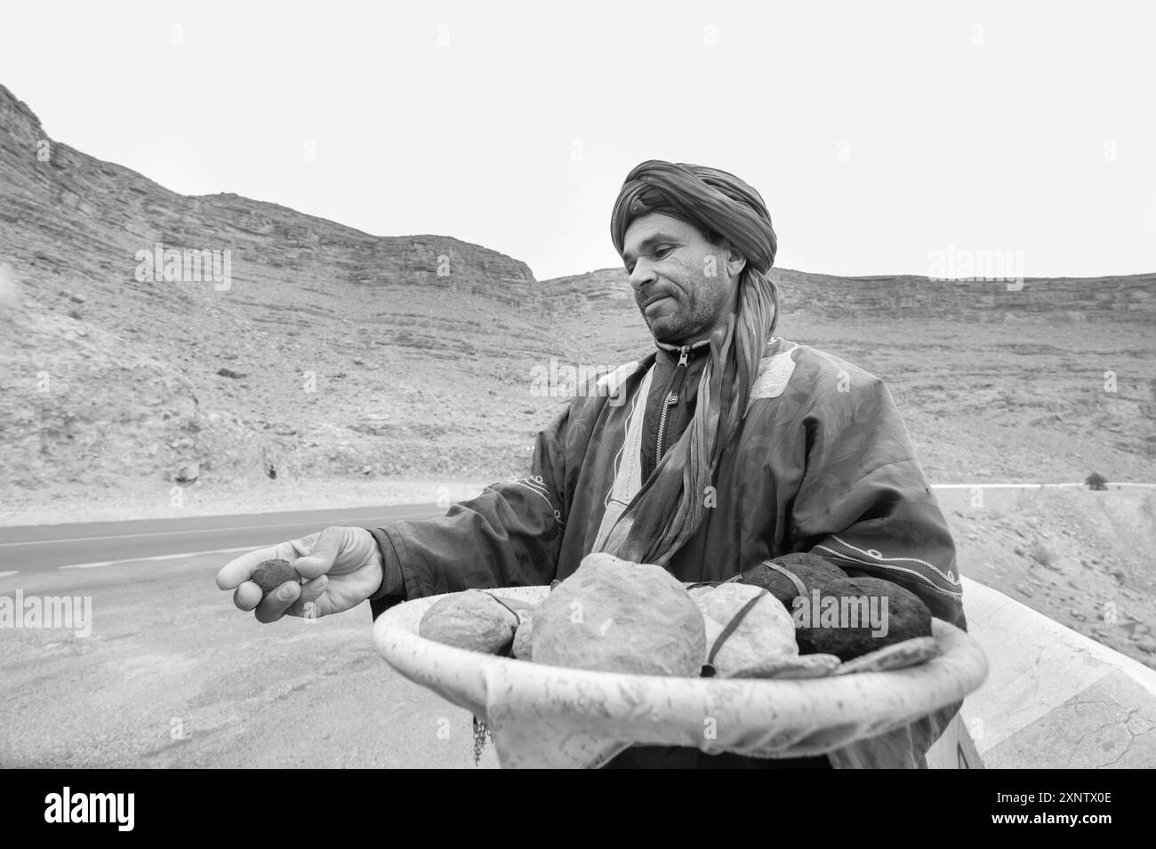 Un vendeur de rue expose ses produits artisanaux et ses fossiles sur le bord de la route qui mène au désert marocain. Il est vêtu d'un costume marocain typique Banque D'Images