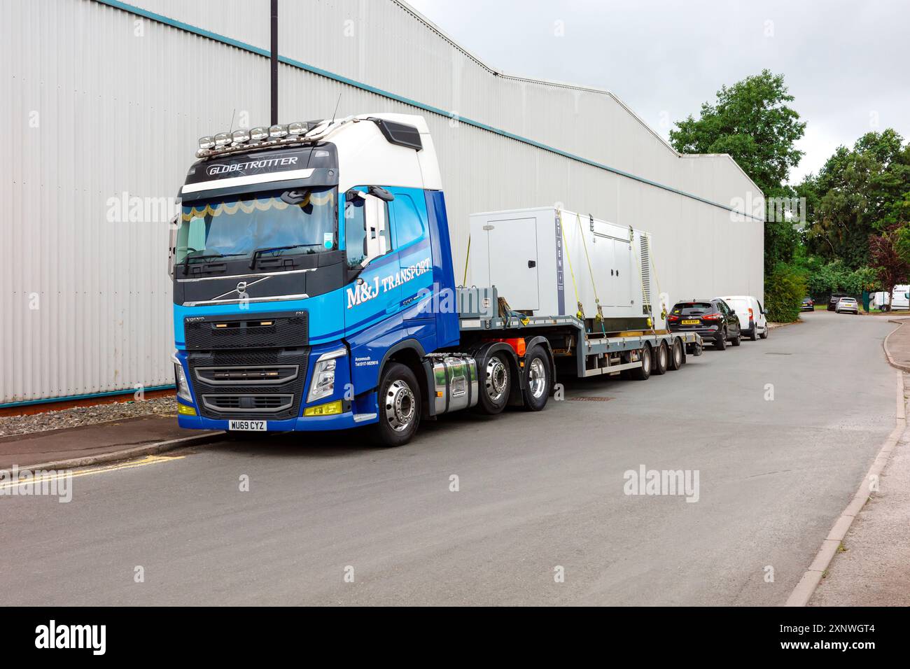 Camion bleu lourd transportant un grand conteneur blanc sur une route industrielle. Trafford Park Manchester Royaume-Uni. Banque D'Images