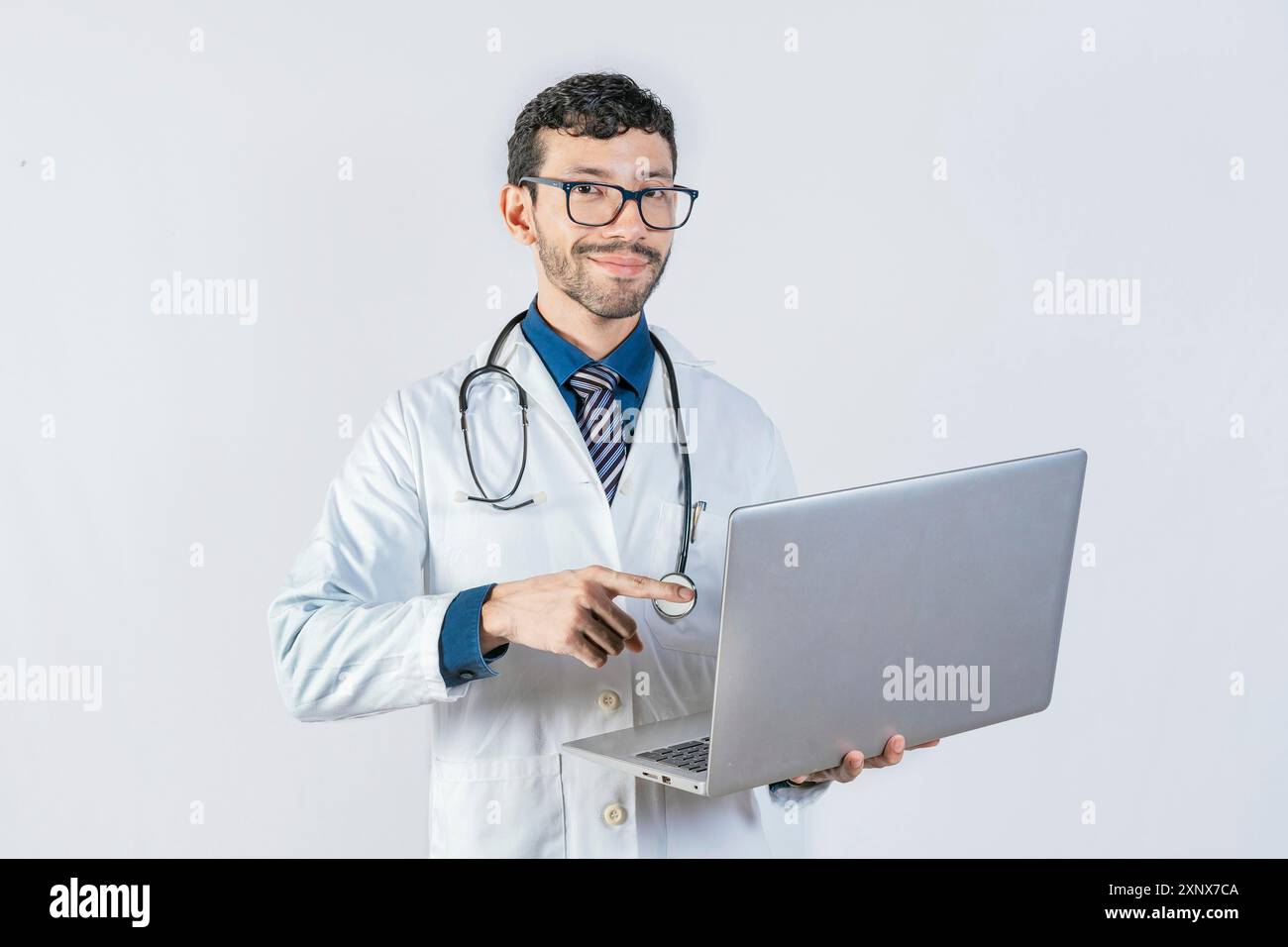 Médecin souriant utilisant et pointant ordinateur portable isolé. Jeune médecin dans des lunettes utilisant un ordinateur portable et regardant l'appareil photo. Beau médecin utilisant un ordinateur portable isolé Banque D'Images