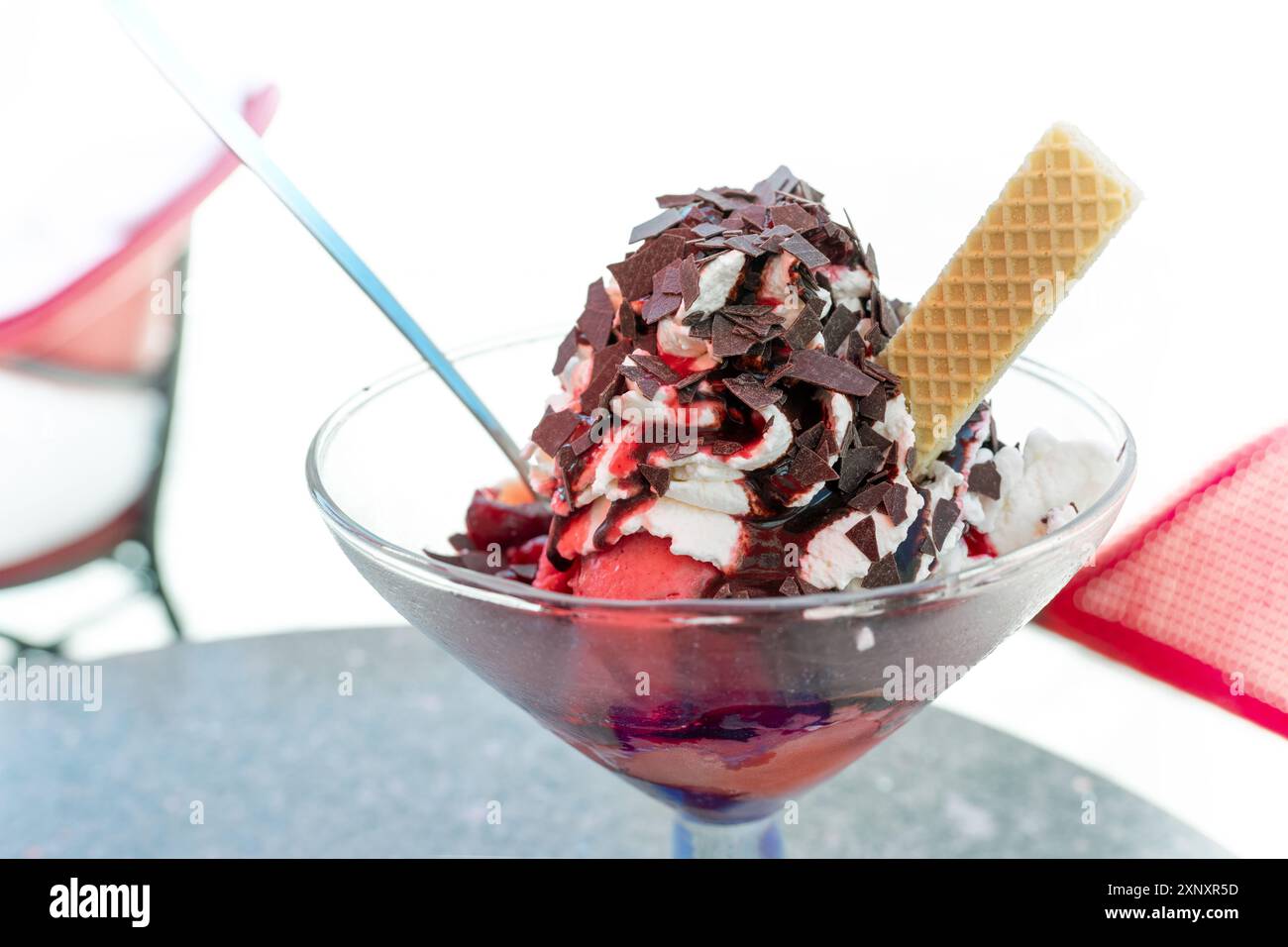Crème glacée sundae avec des cuillères à la vanille et aux cerises, crème fouettée, sauce aux fruits rouges et pépites de chocolat dans un café de rue sur une chaude journée d'été dans la ville, Banque D'Images