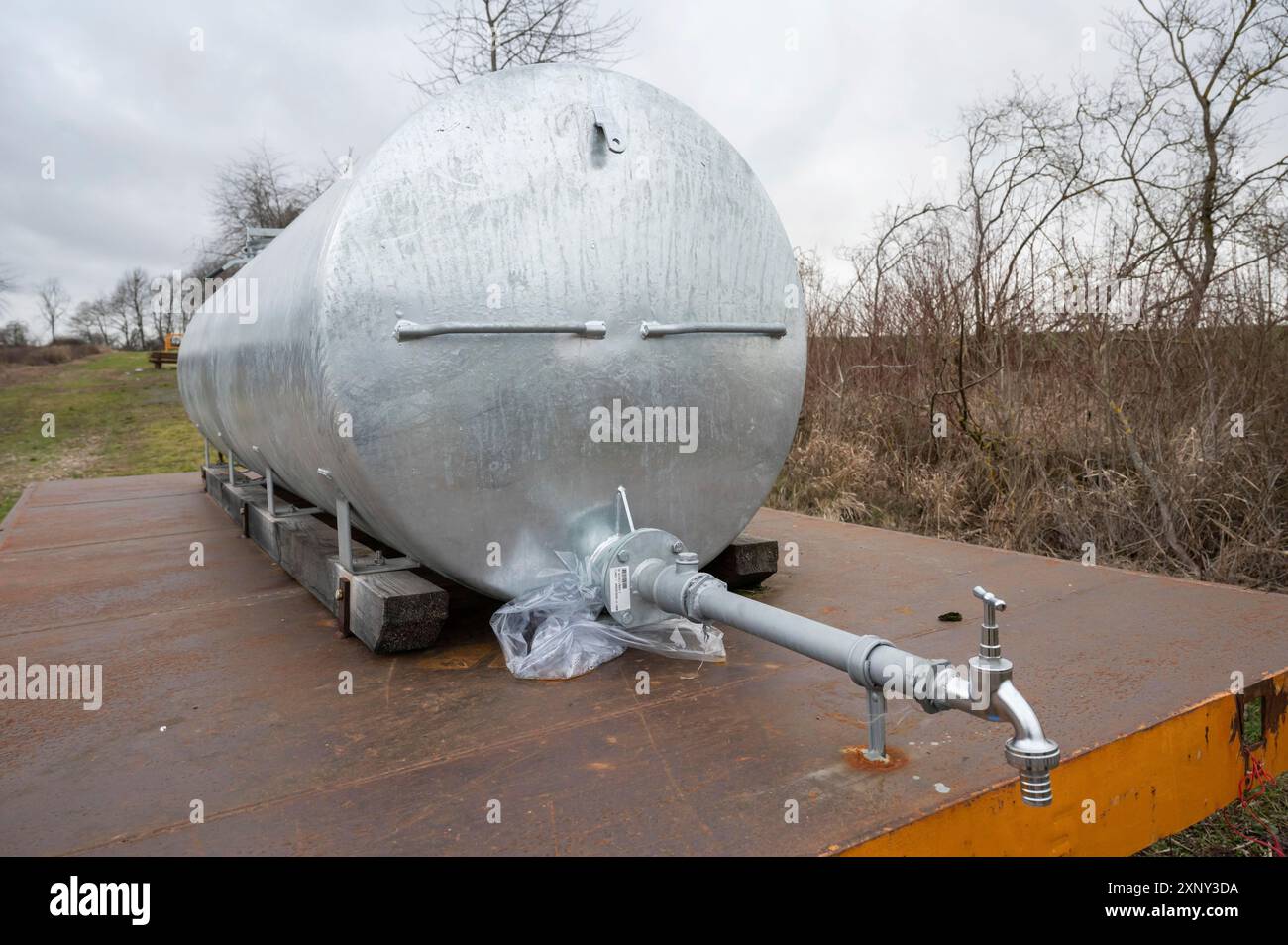 Réservoir d'eau en métal argenté avec pompe à eau à l'avant sur une remorque à l'extérieur à côté d'un champ agricole Banque D'Images