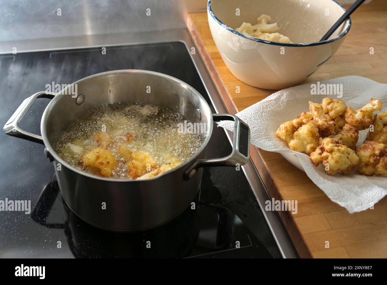 Chou-fleur frit en cours, frire dans de l'huile de cuisson chaude dans une casserole, sécher sur une serviette en papier et cru dans un bol, préparation d'une collation végétarienne Banque D'Images