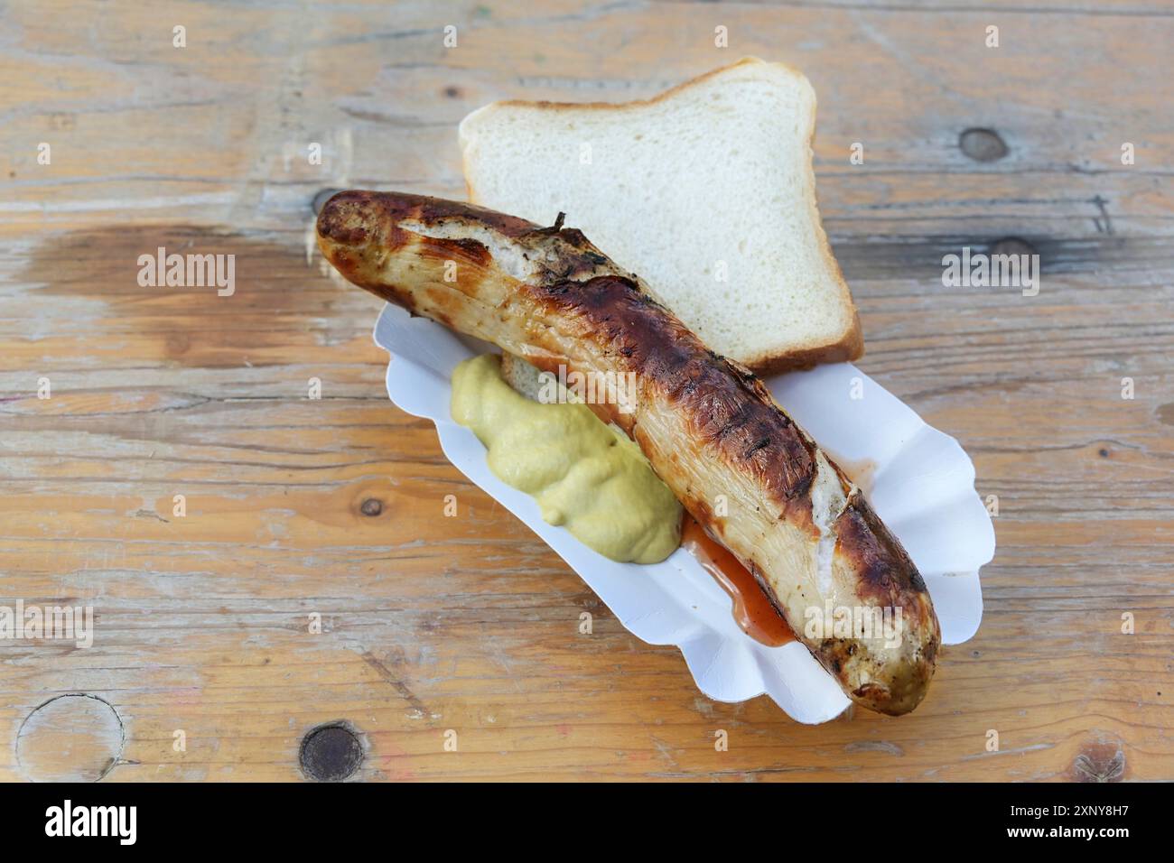 Saucisse rôtie ou bratwurst allemand sur une assiette en papier avec de la moutarde et du pain sur une vieille table en bois, restauration rapide typique en plein air sur un événement de vacances Banque D'Images