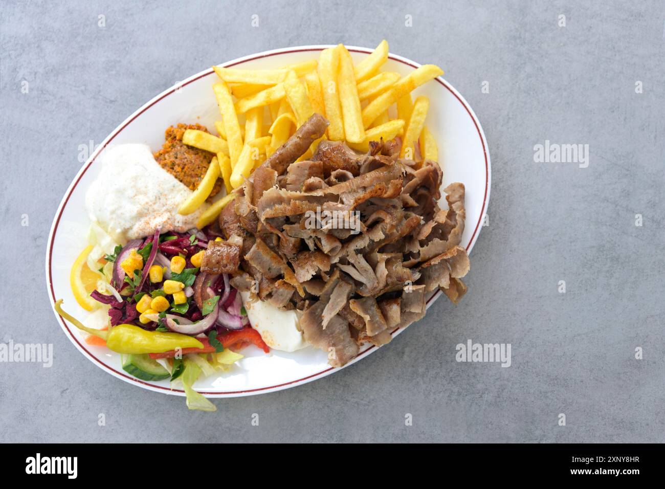 Doner kebab, tranches de viande d'une brochette rotative avec salade, frites et sauce trempette au yogourt sur une assiette ovale et une table grise, espace copie, haut Banque D'Images