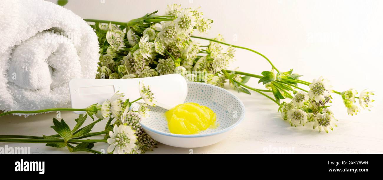 Hydratant cosmétique ou émollient et une spatule pour pédicure et peau douce des pieds dans un petit bol et quelques fleurs vertes sur un fond de bois clair Banque D'Images