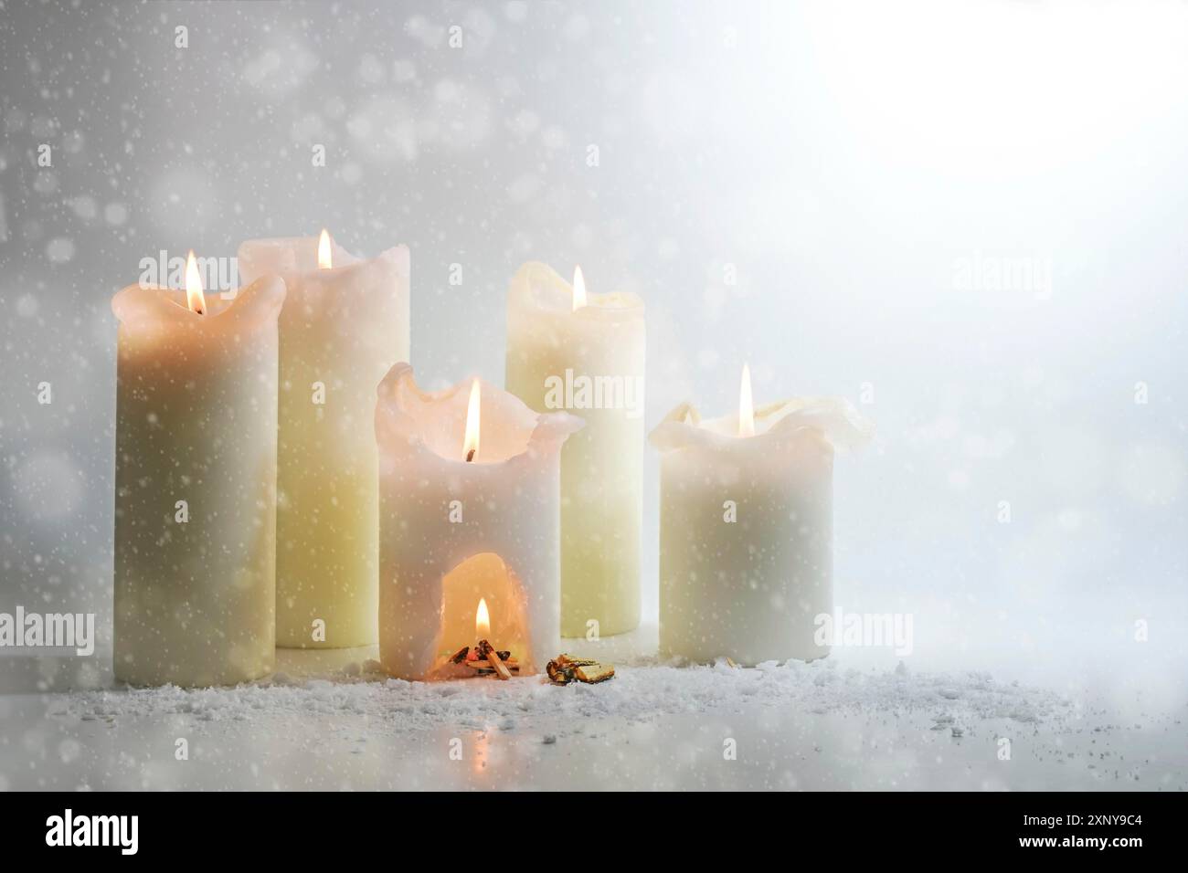 Bougies blanches brûlant dans la neige, dans l'un est une sculpture avec un feu de camp chaud, nature morte hivernale surréaliste, concept de chaleur et d'énergie, fond gris clair Banque D'Images