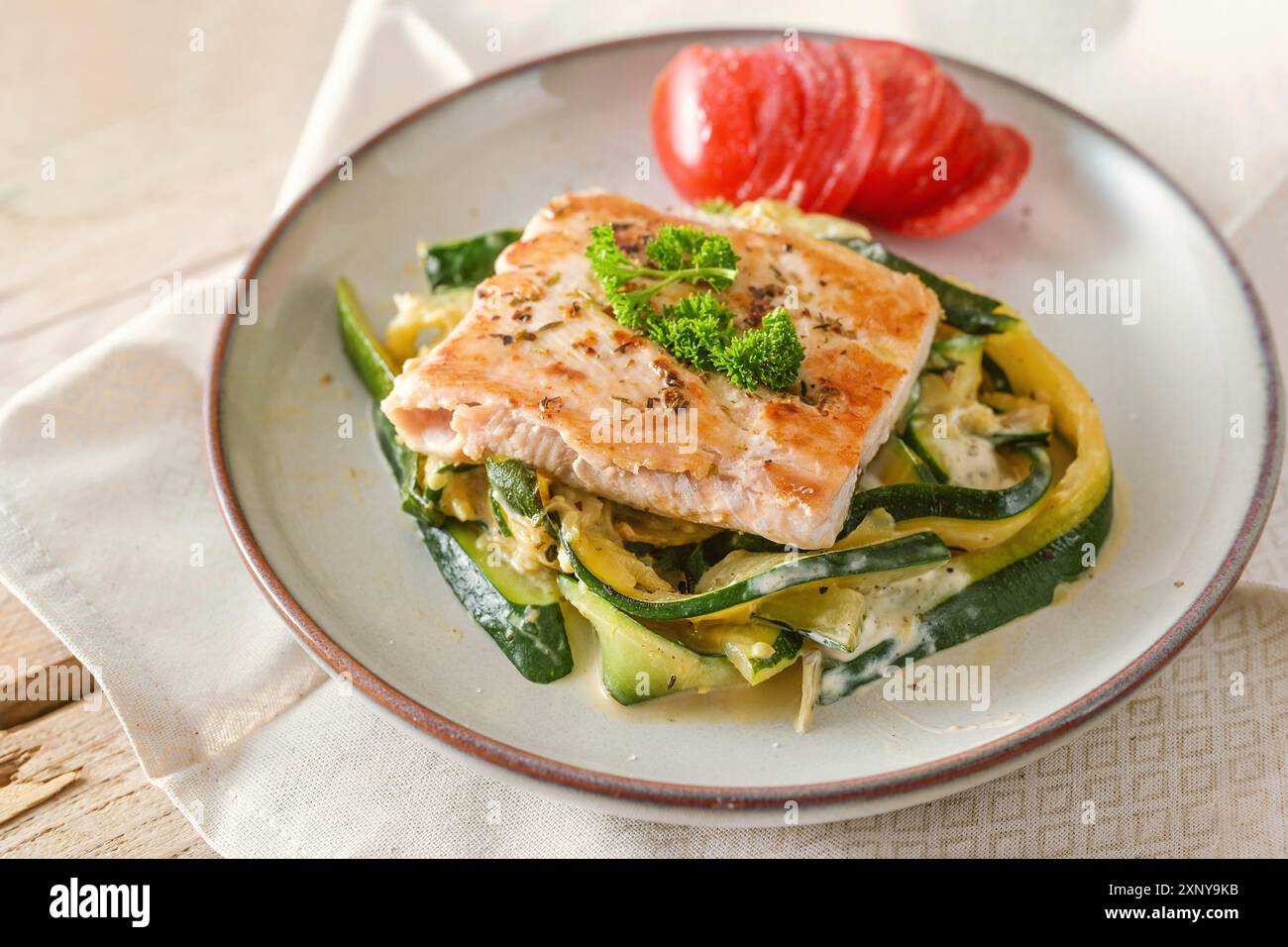 Saumon sauvage frit avec garniture de persil sur les légumes de courgettes et de tomate fraîche sur une assiette légère, repas sain pour un régime pauvre en glucides, focus sélectionné Banque D'Images