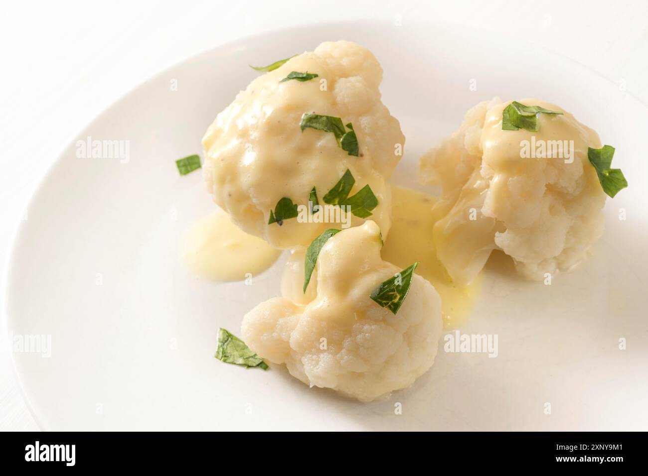 Chou-fleur cuit avec sauce hollandaise et garniture de persil sur une assiette blanche, plat d'accompagnement de légumes, espace de copie, foyer choisi, profondeur de champ étroite Banque D'Images