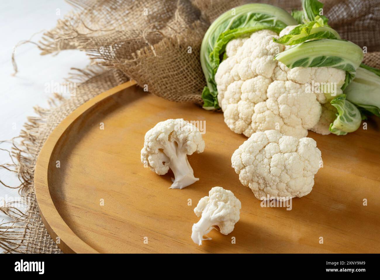 Chou-fleur frais et quelques morceaux ou bouquets sur toile de jute rustique et un plateau en bois, légumes sains et ingrédient de cuisine, espace de copie, sélectionné Banque D'Images