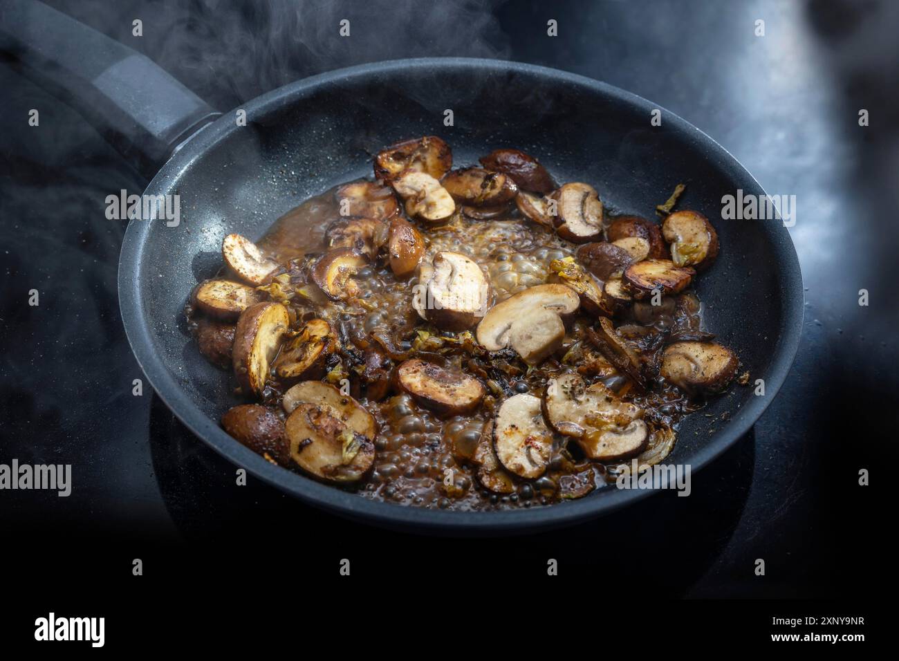 Les champignons avec de la sauce sont cuits dans une poêle noire vapeur sur la table de cuisson, préparant un repas végétarien, espace de copie, foyer sélectionné, profondeur étroite Banque D'Images