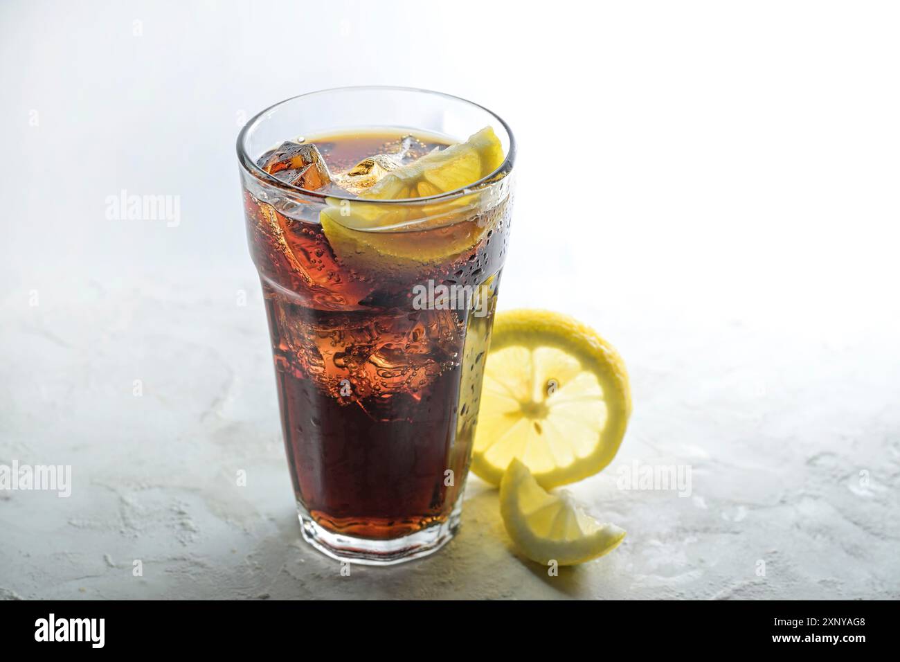 Cola frais avec des glaçons et des tranches de citron dans un verre à boire, boisson de caféine sucrée sur un fond gris clair, espace de copie, foyer sélectionné Banque D'Images