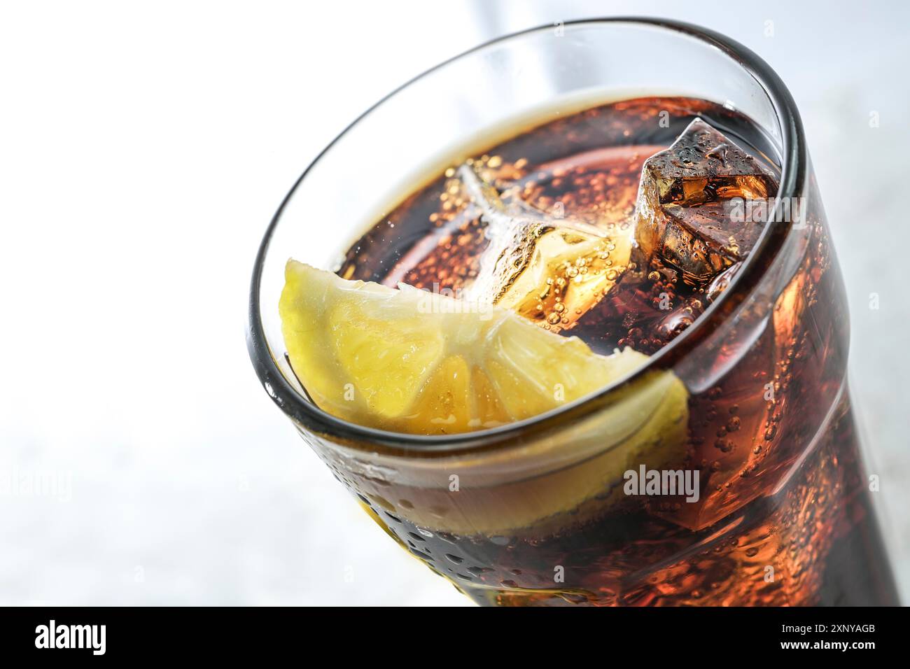 Partie d'un verre à boire avec du cola frais, des glaçons et une tranche de citron, boisson rafraîchissante de caféine sucrée sur un fond gris clair, espace de copie Banque D'Images