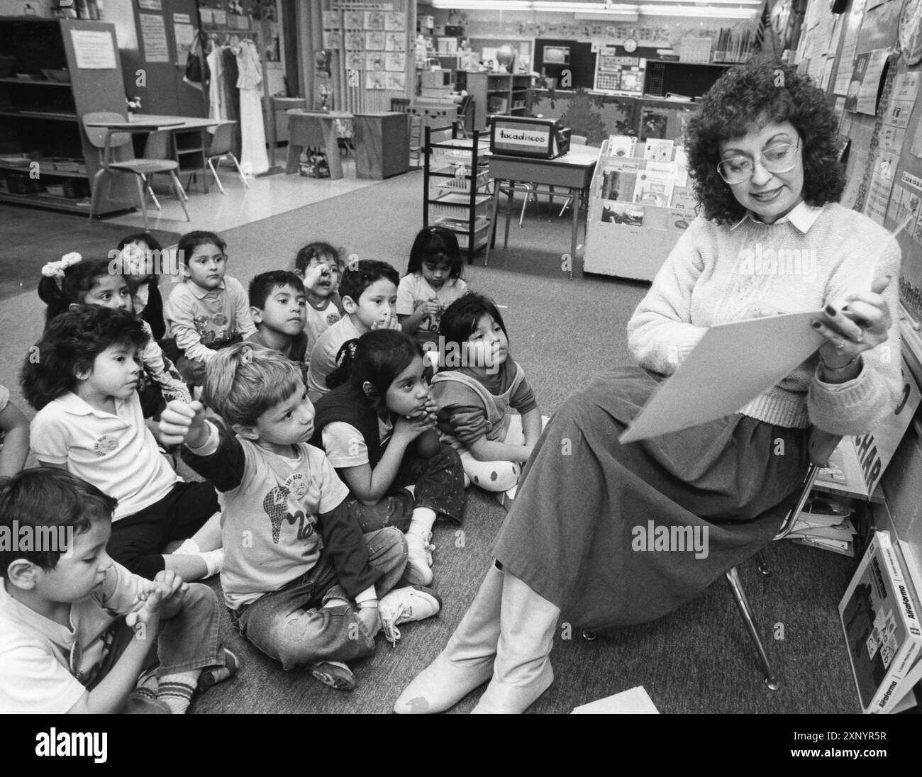 Austin Texas USA, 1990 : une enseignante hispanique de maternelle est assise sur une chaise tout en lisant un livre d'images à ses élèves hispaniques assis autour d'elle sur le sol. ©Bob Daemmrich Banque D'Images