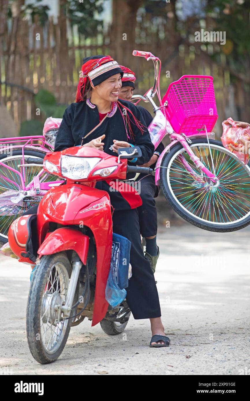 Une femme vietnamienne en costume traditionnel de la minorité Dao transporte un vélo rose sur un cyclomoteur, Nam Dam Dao Cultural Village, Ha Giang Banque D'Images